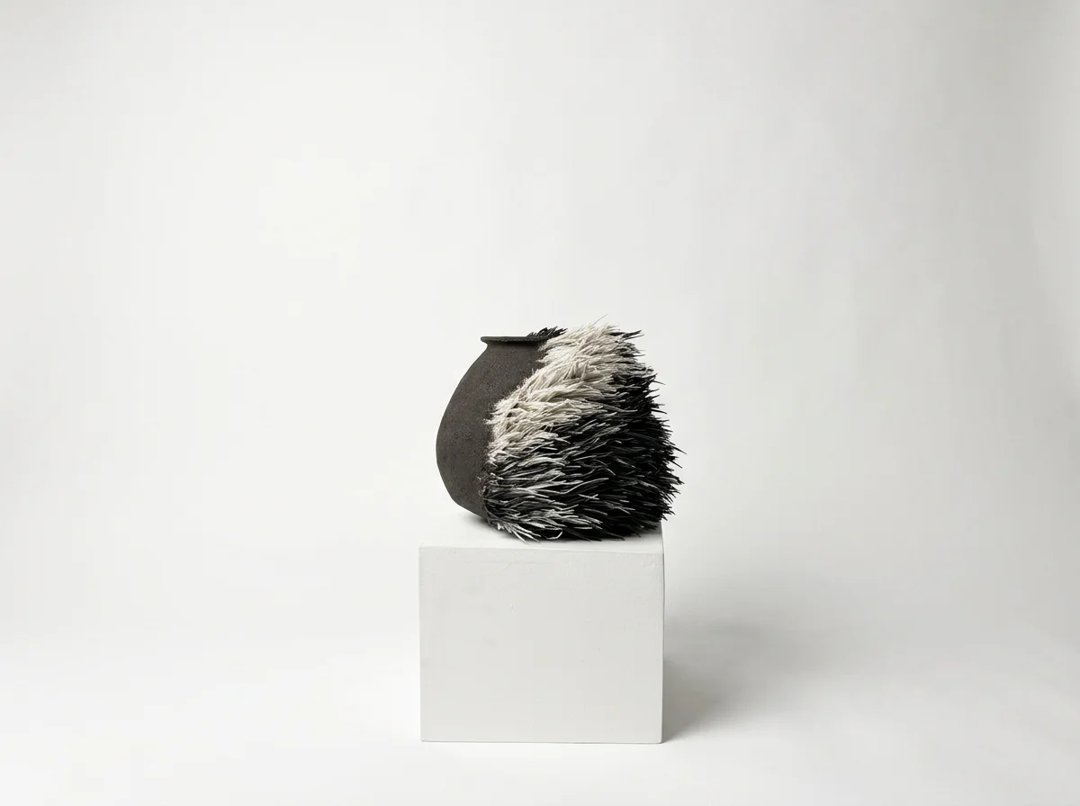 Vase noir avec une partie de poils en porcelaine blancs et noirs placé sur un piédestal blanc, fond blanc