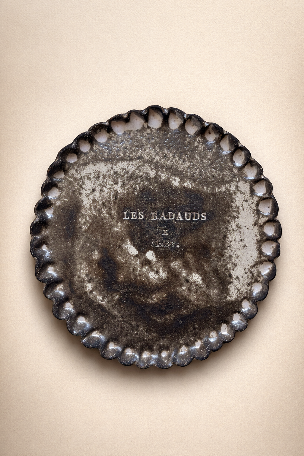 une assiette en grès avec l'inscription 'LES BADAUDS' , entourée d'une bordure festonnée