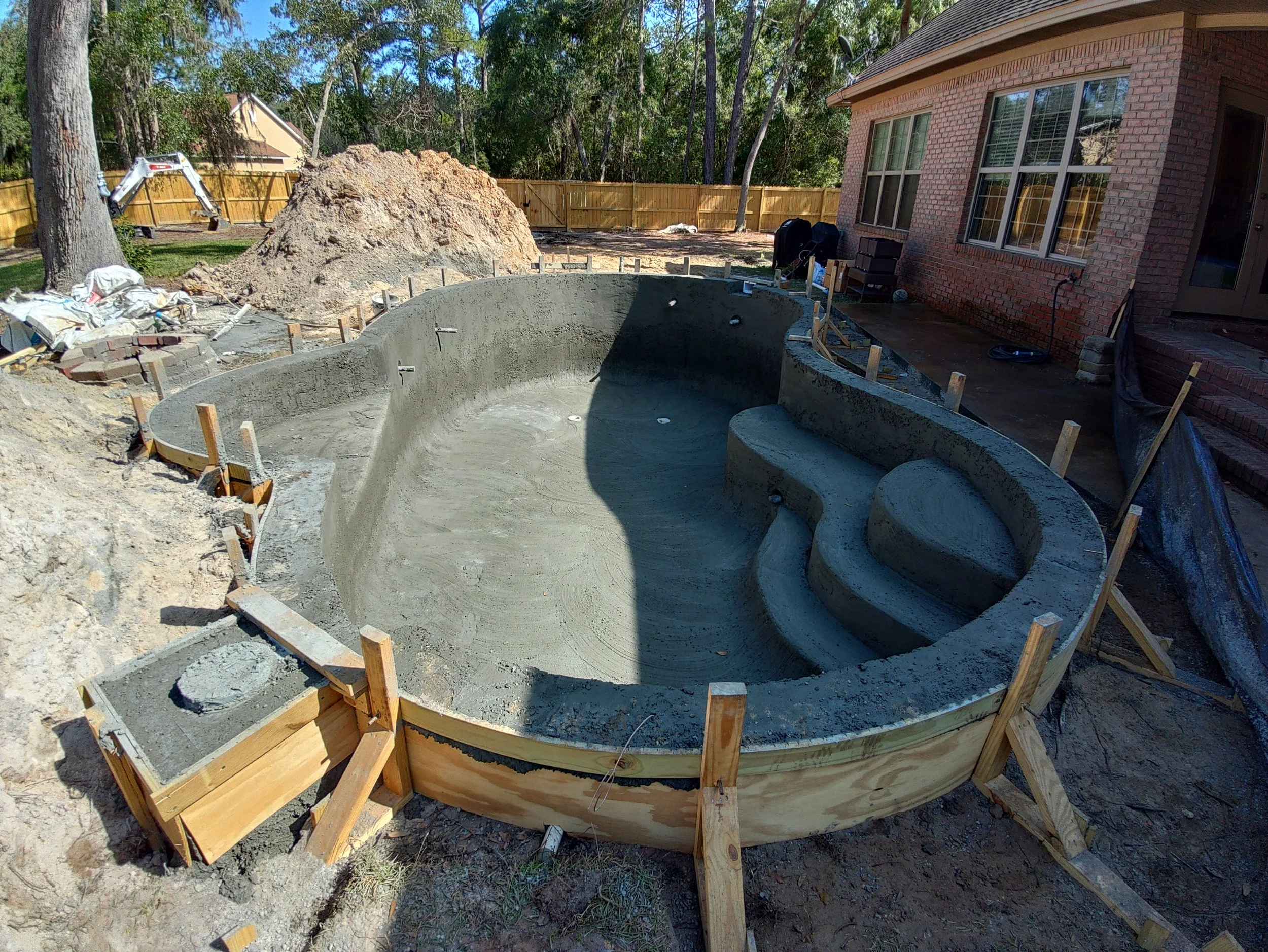 Under-construction swimming pool in backyard with wooden forms and construction materials around