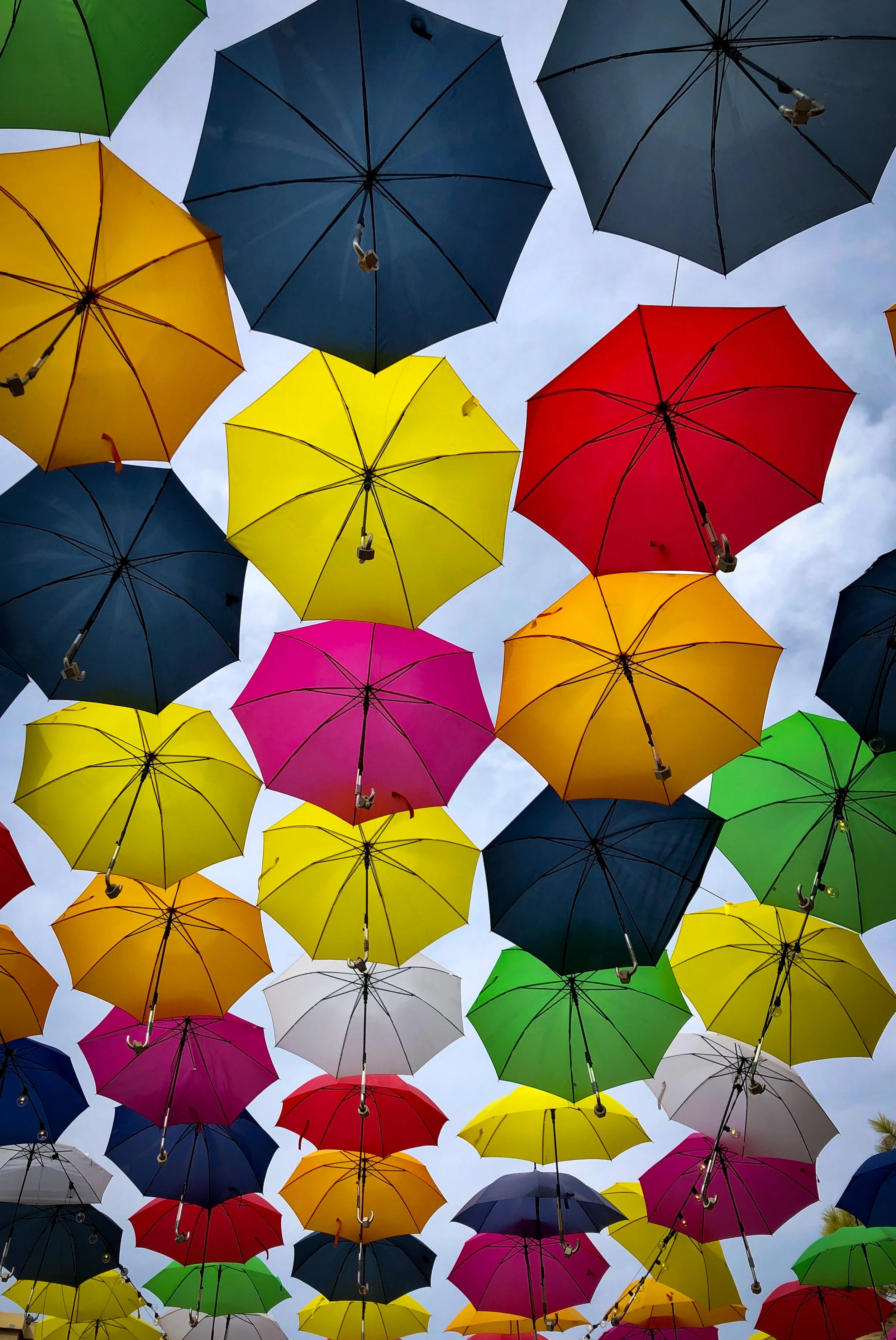 Colorful umbrellas suspended upside-down overhead against a cloudy sky.
