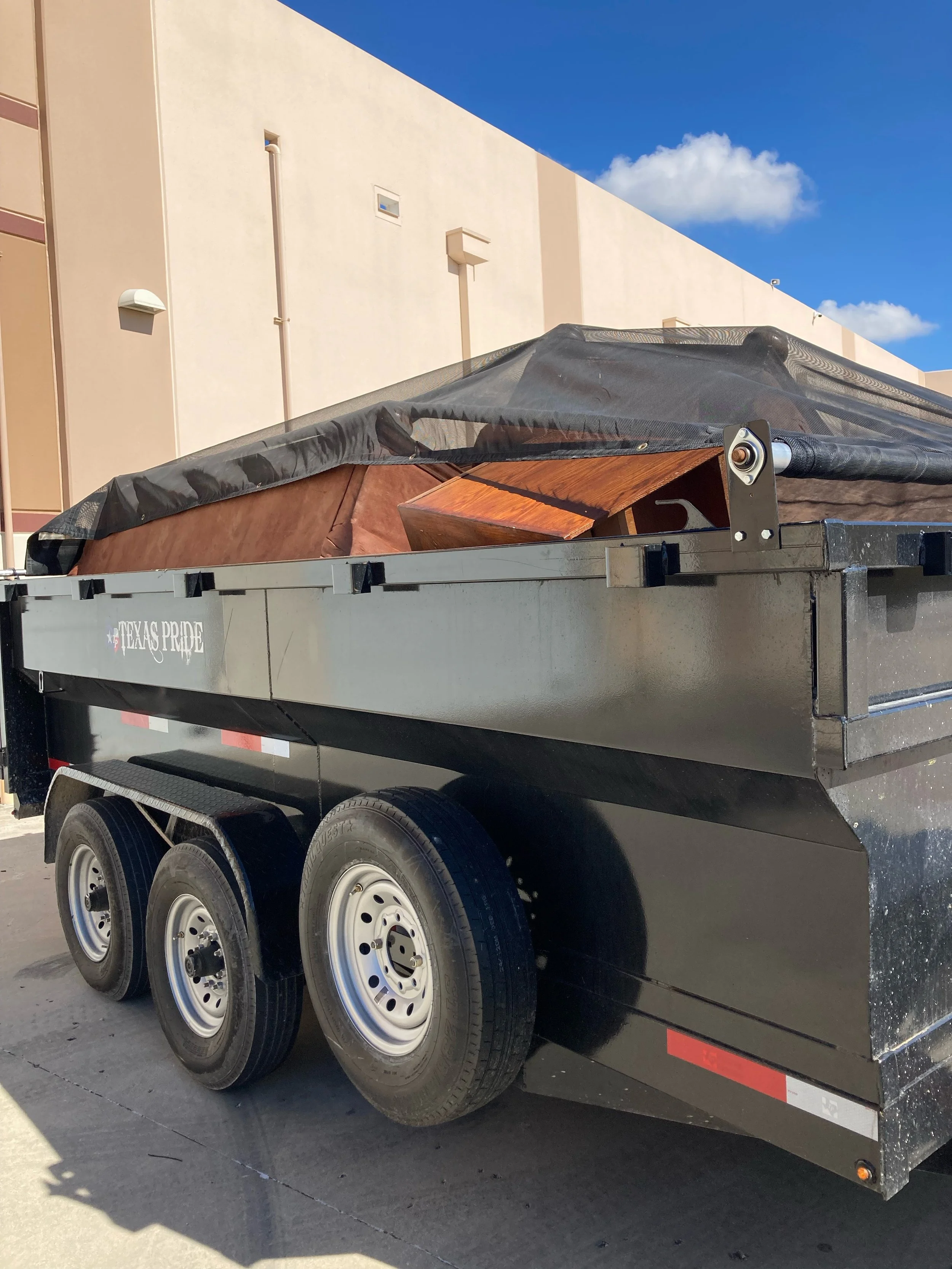 A black trailer carrying a small boat and a canopy in an outdoor setting with a beige building and blue sky in the background.