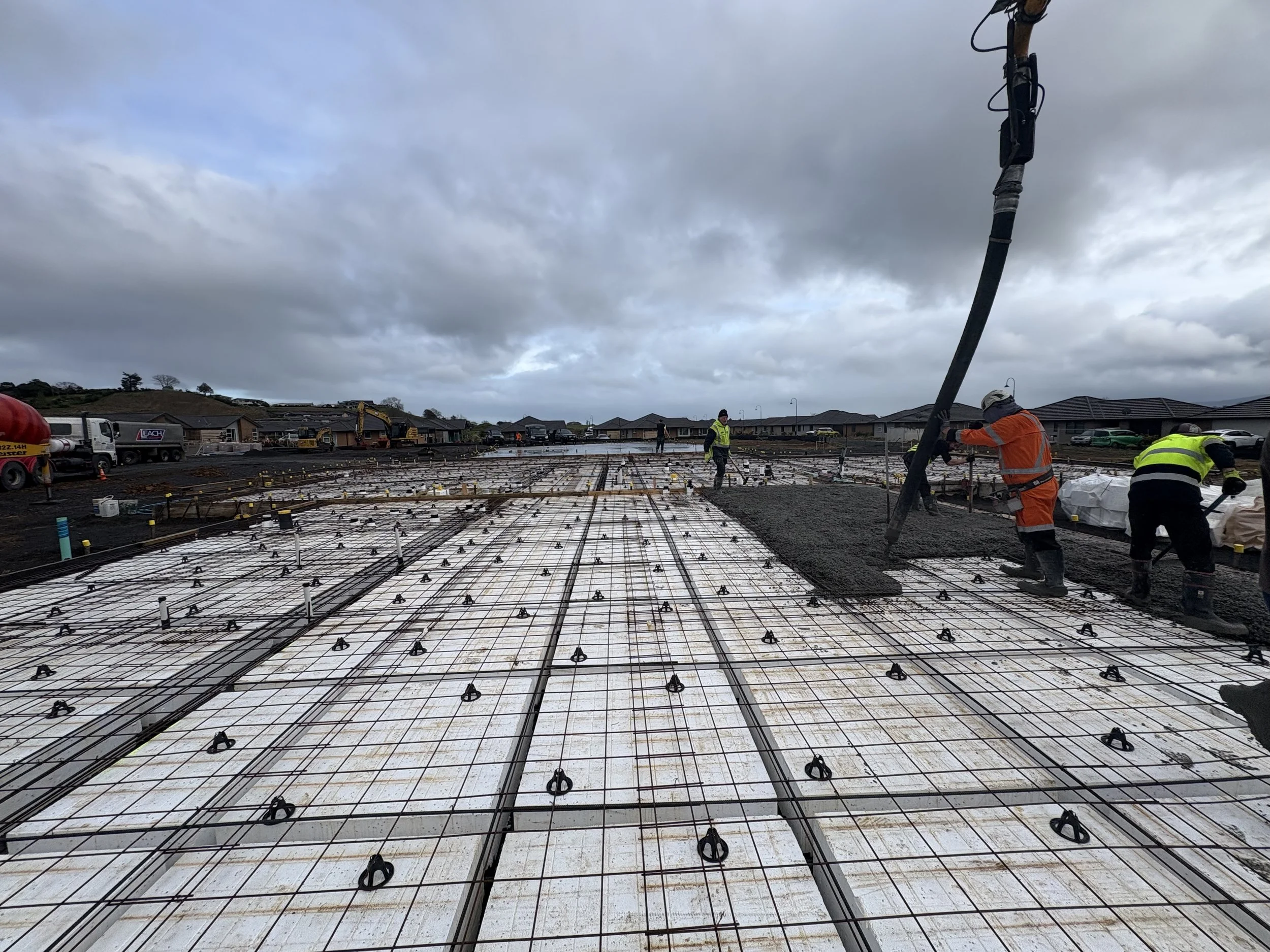 Construction workers pouring concrete over rebar framework for a building foundation with cloudy sky overhead.
