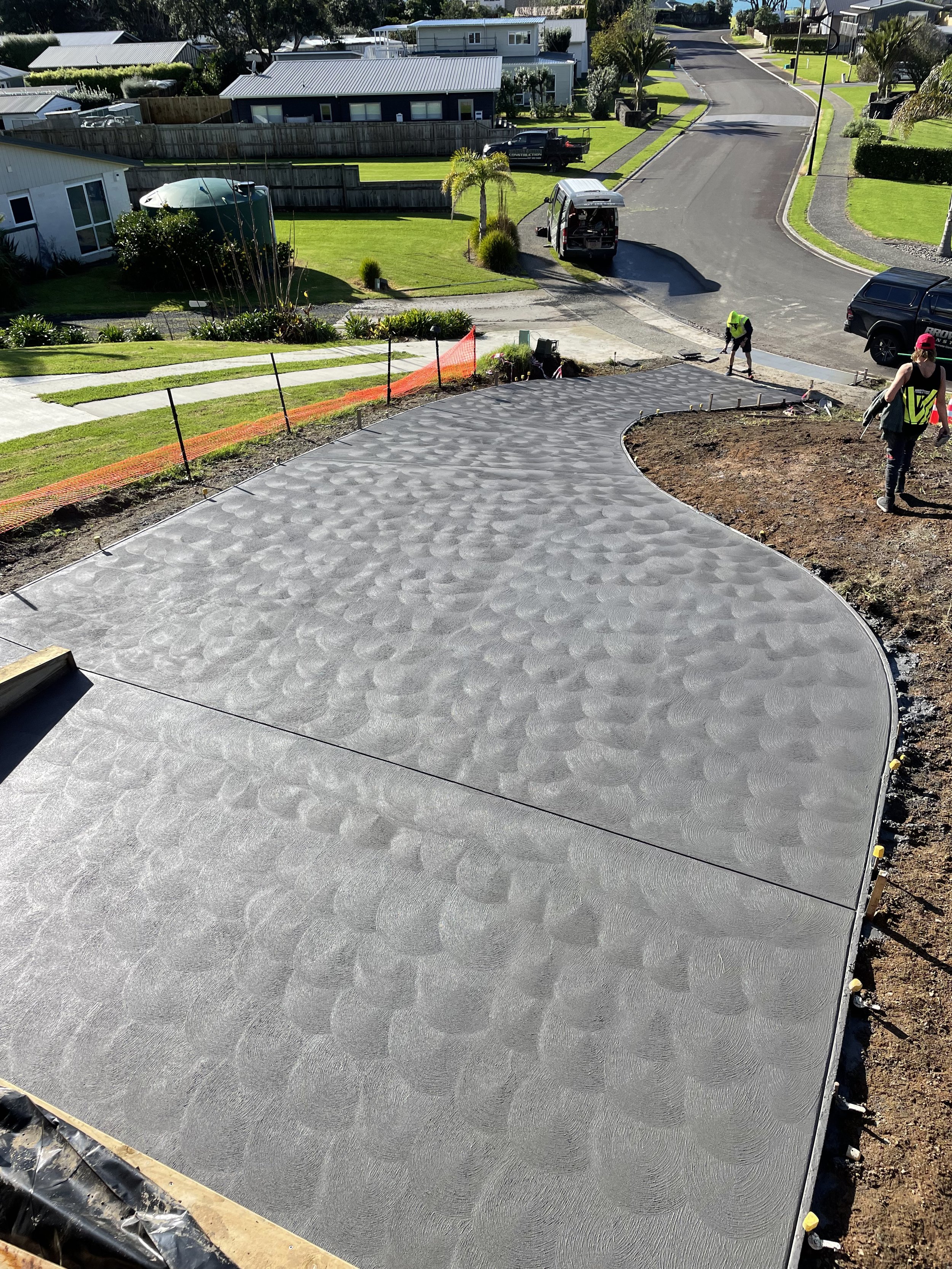 Concrete driveway with textured pattern being poured and smoothed by construction workers in a residential neighborhood.