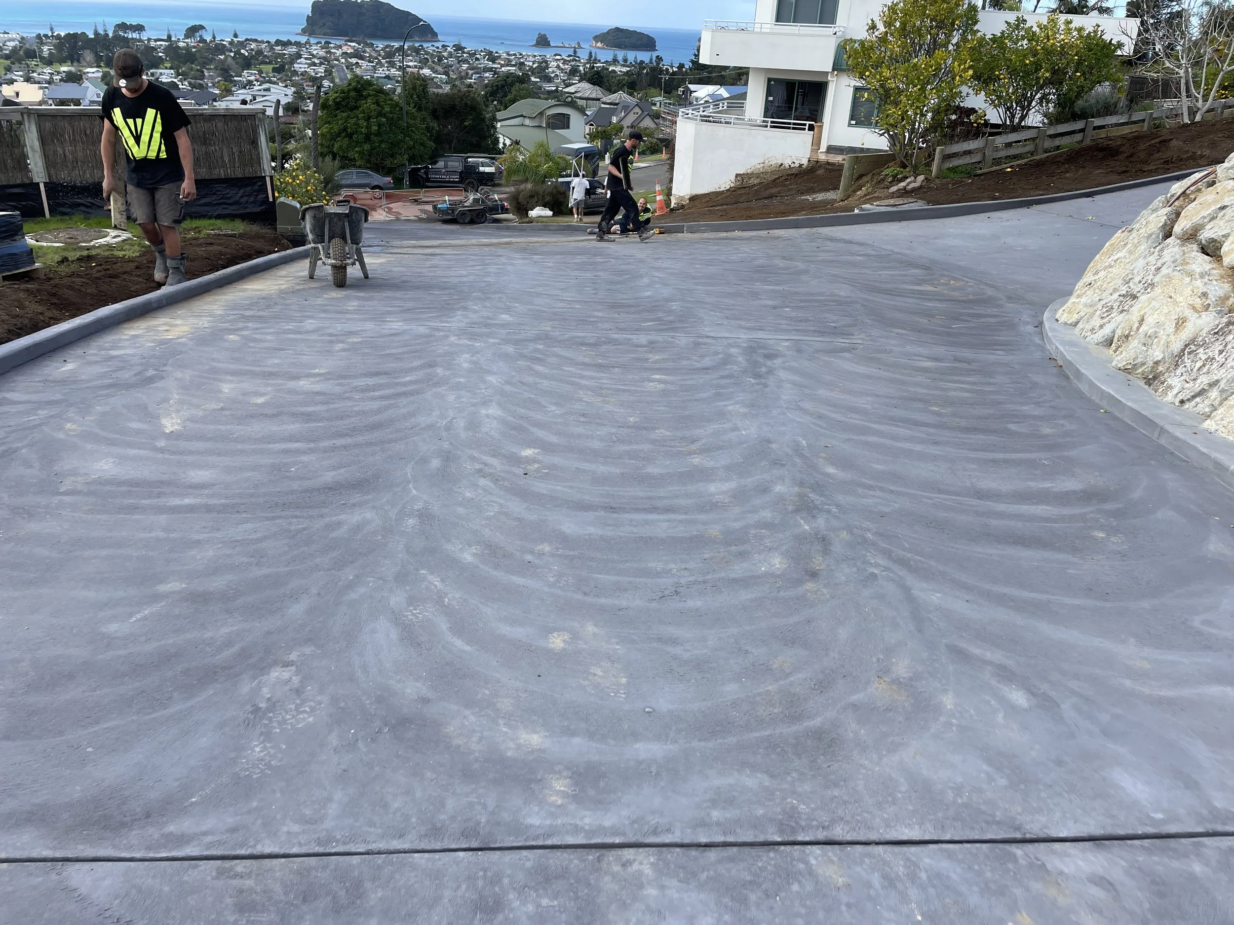 Construction workers pouring and leveling concrete on a driveway with hills and houses in the background