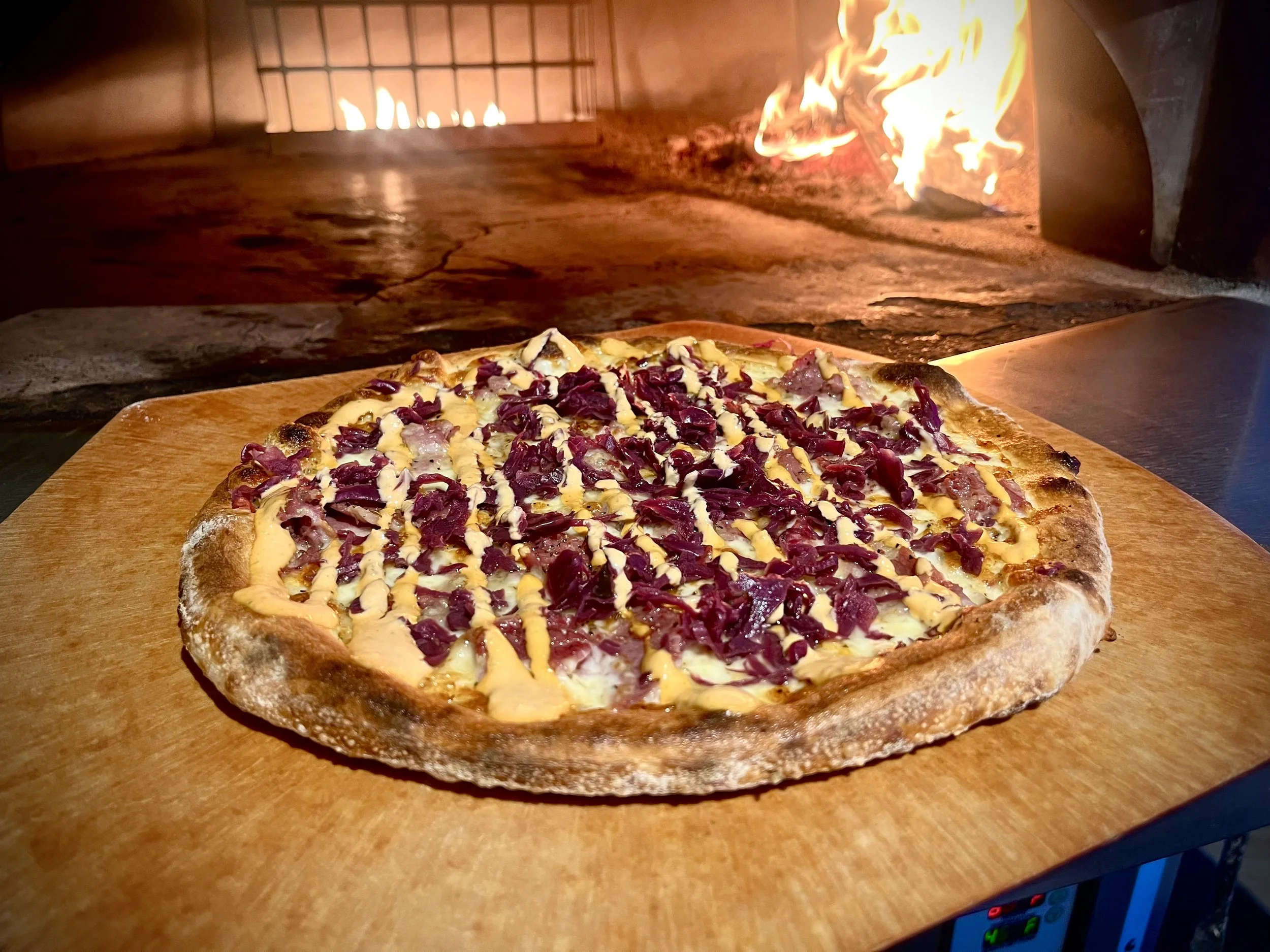 Un pizza con queso y tocino en un horno de leña.