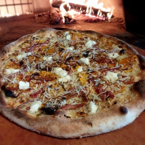 Pizza with cheese, meat, and vegetables in front of a lit fireplace.