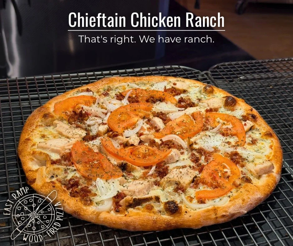 A freshly baked chieftain chicken ranch pizza with a golden crust, topped with chicken, sliced tomatoes, onions, and melted cheese on a cooling rack.