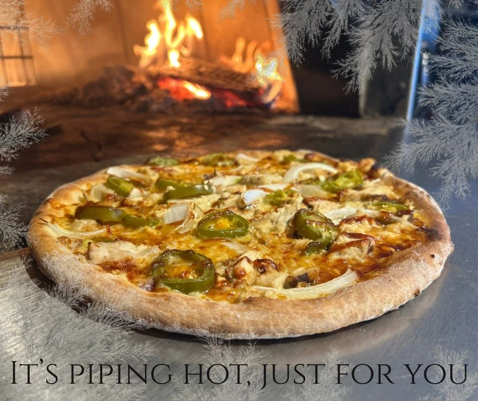A pizza topped with jalapenos, onions, and cheese in front of a fireplace with a Christmas-themed border and the caption "It's piping hot, just for you."