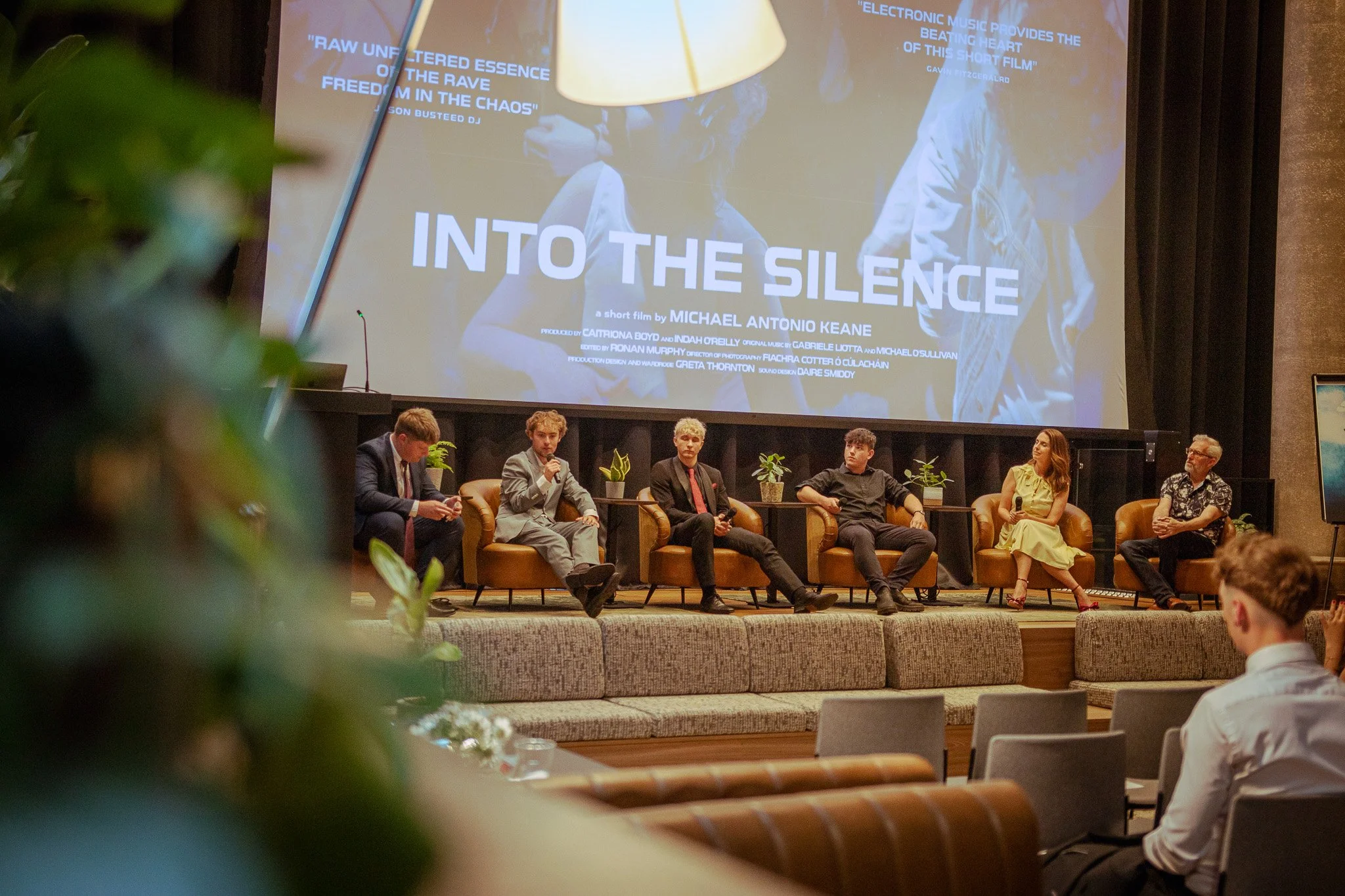 Panel discussion at a film event, with five people seated on stage in front of a large screen displaying the movie title 'Into the Silence' and credits, and an audience watching.