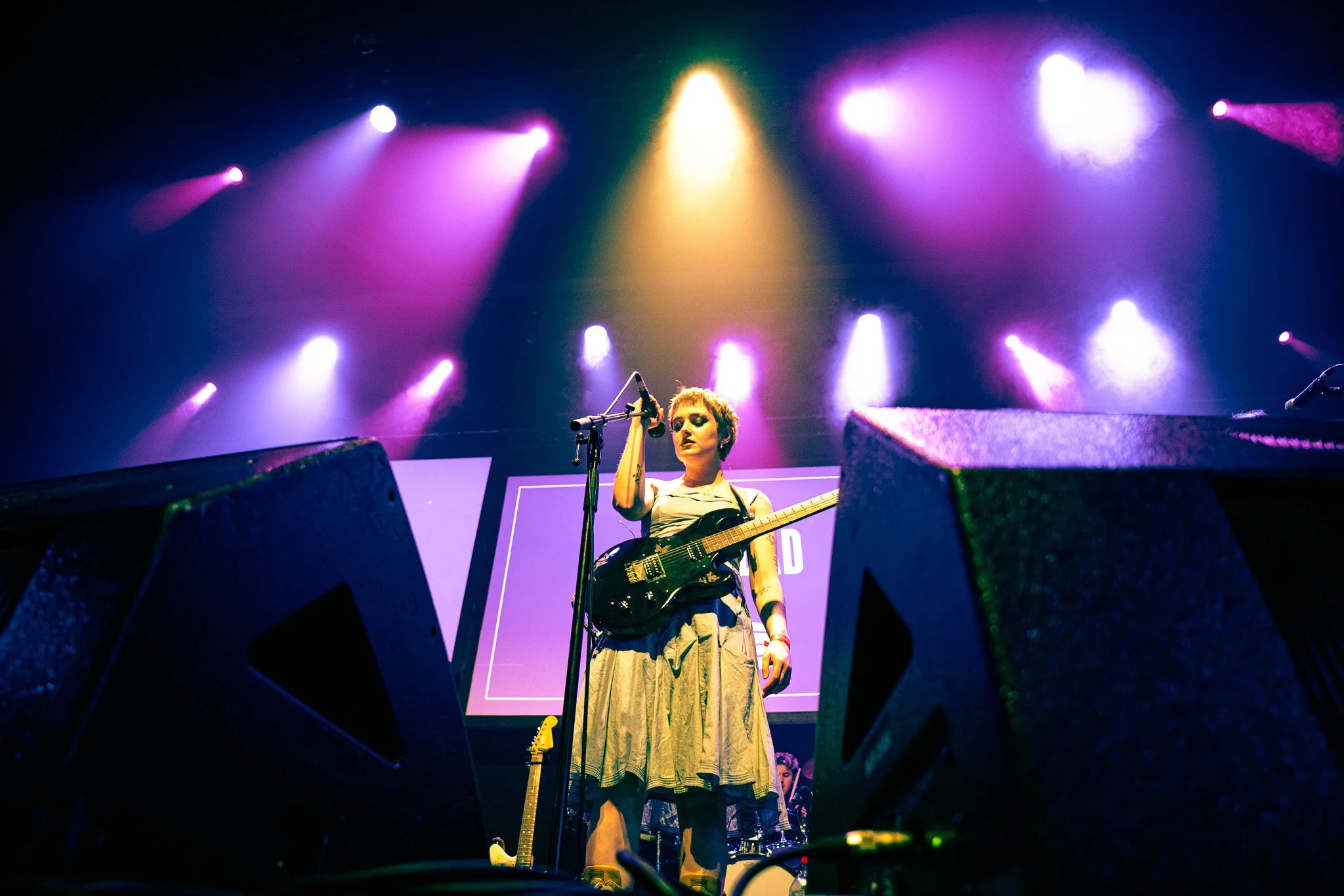 A musician on stage playing an electric guitar during a concert with a large screen behind displaying the word 'NEWDAD' and colorful lighting overhead. Photography coverage at the RTE Music Choice Awards. 