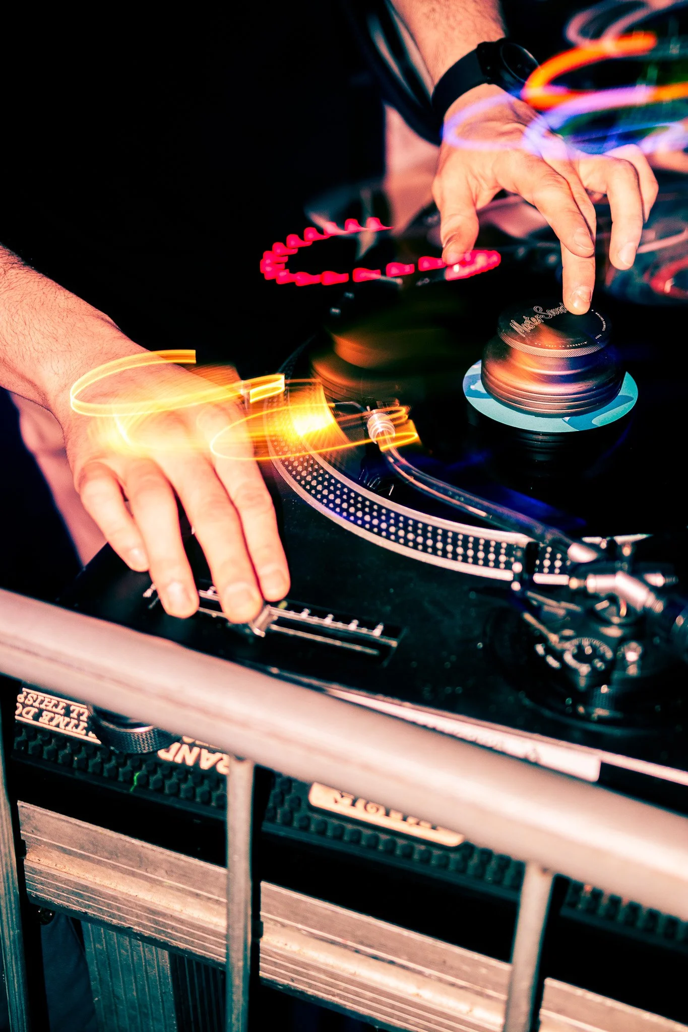 A DJ is mixing music on turntables at a club, with colorful light trails creating a vibrant atmosphere. Childsmind, Irish DJ.