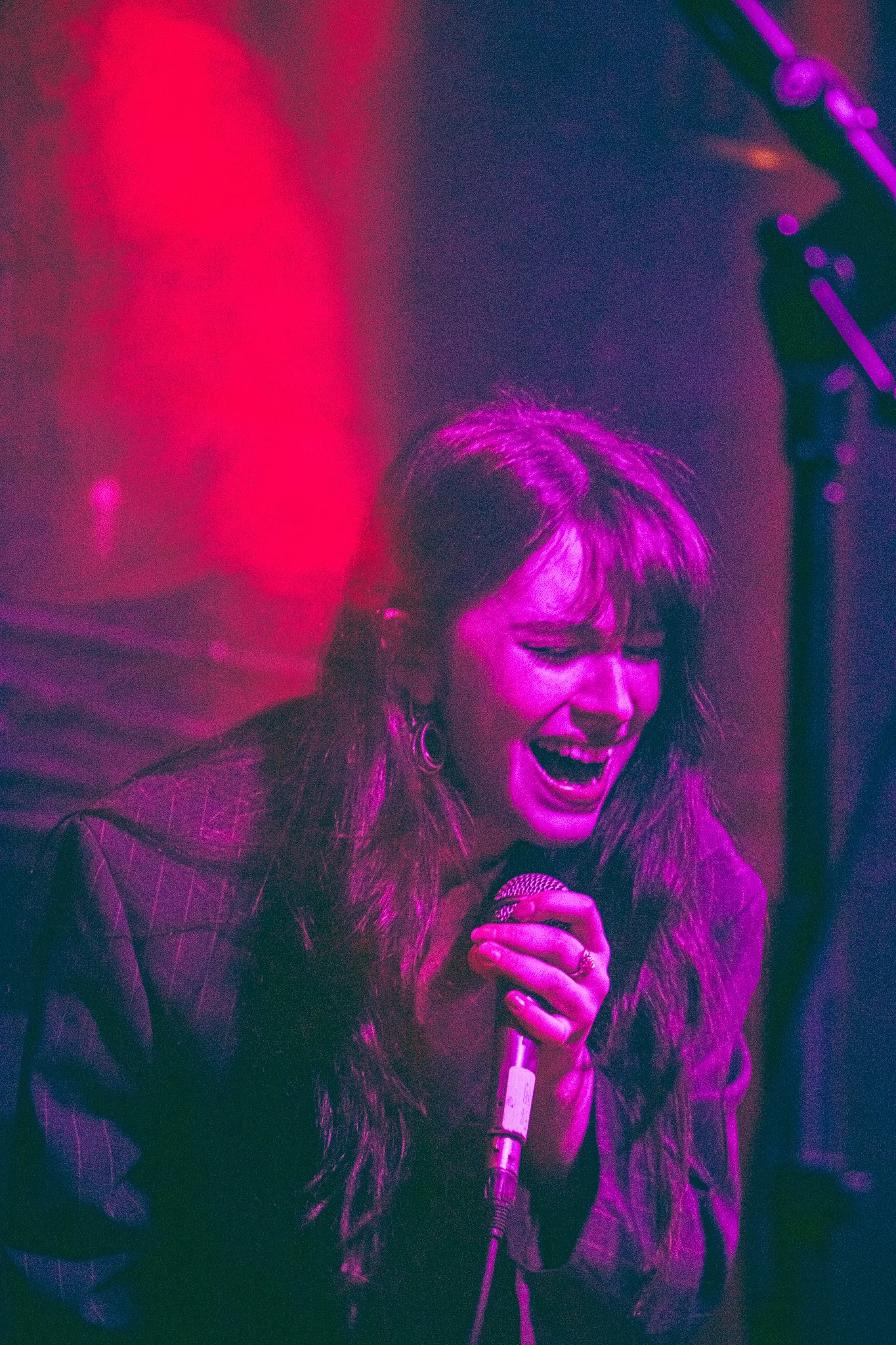 Florence Road Member Lily Aaron performing in The Academy. A woman with long hair singing passionately into a microphone, illuminated by purple and pink stage lighting. irish Music Photography.