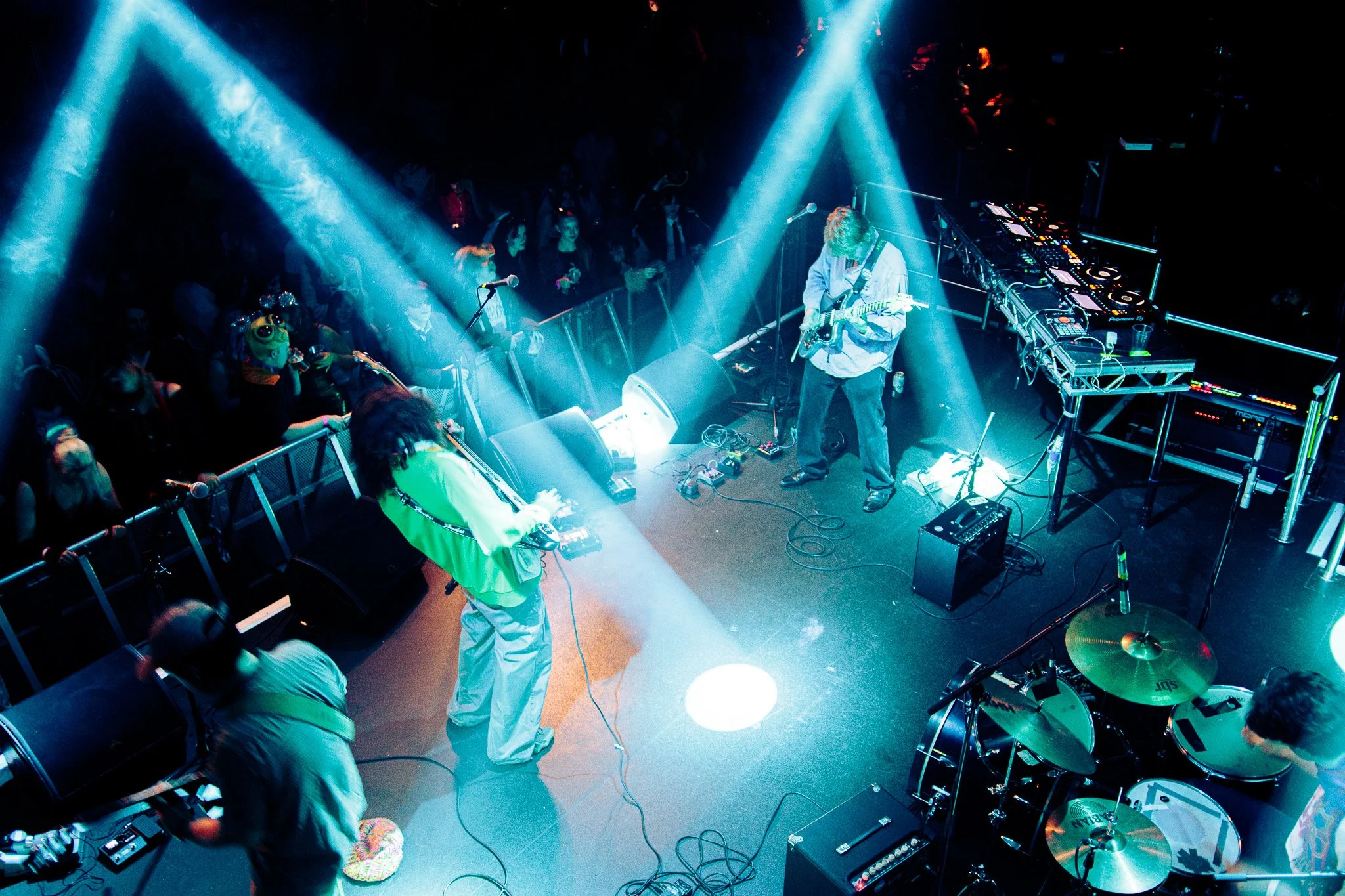 Musicians performing on a stage with dramatic blue and white lighting, audience watching from the front