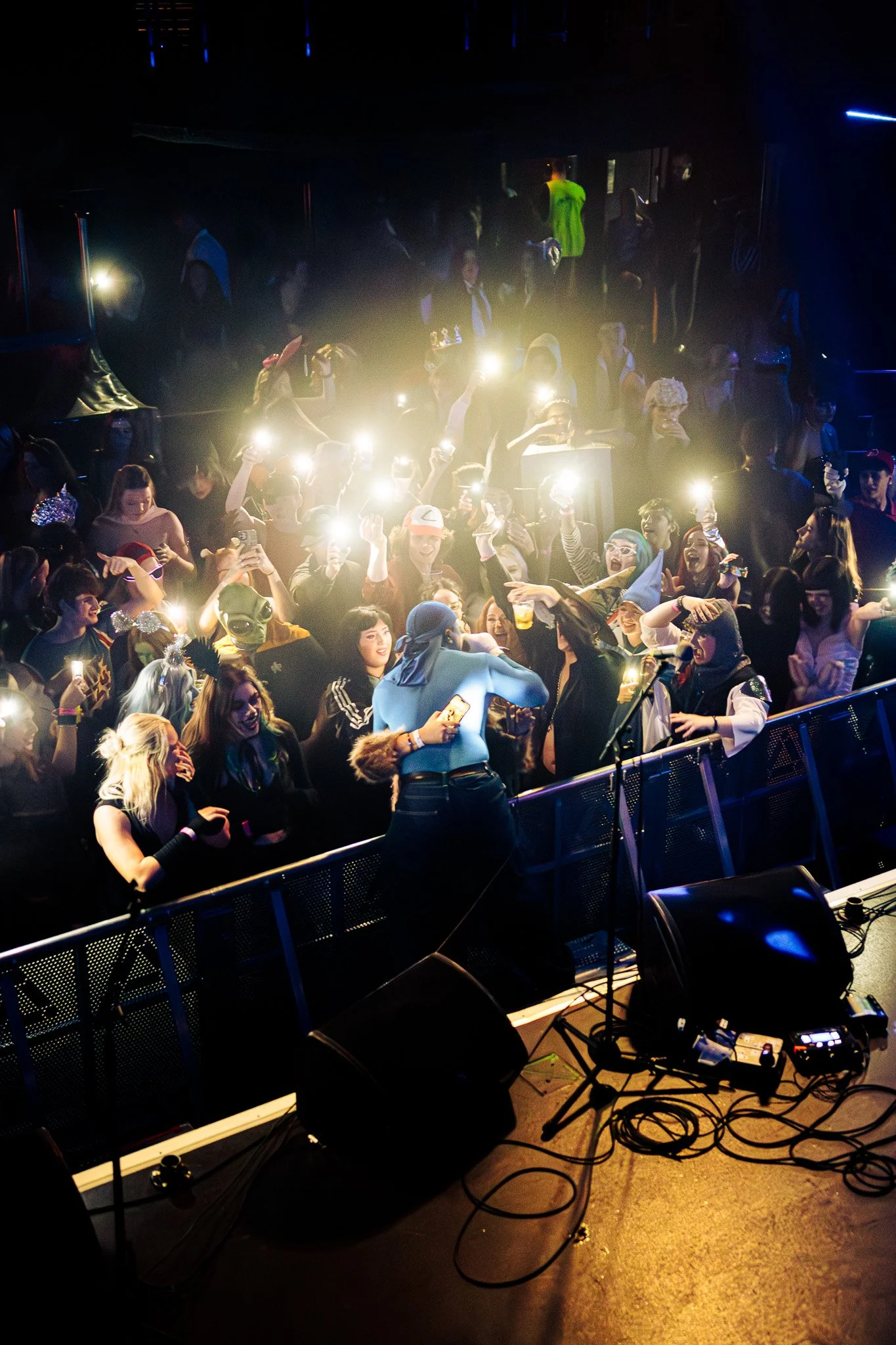 People at a concert dance and take photos with flashlights on their phones. The scene is lively, with some individuals wearing costumes. Irish musician, the olympia theatre. 2025. 