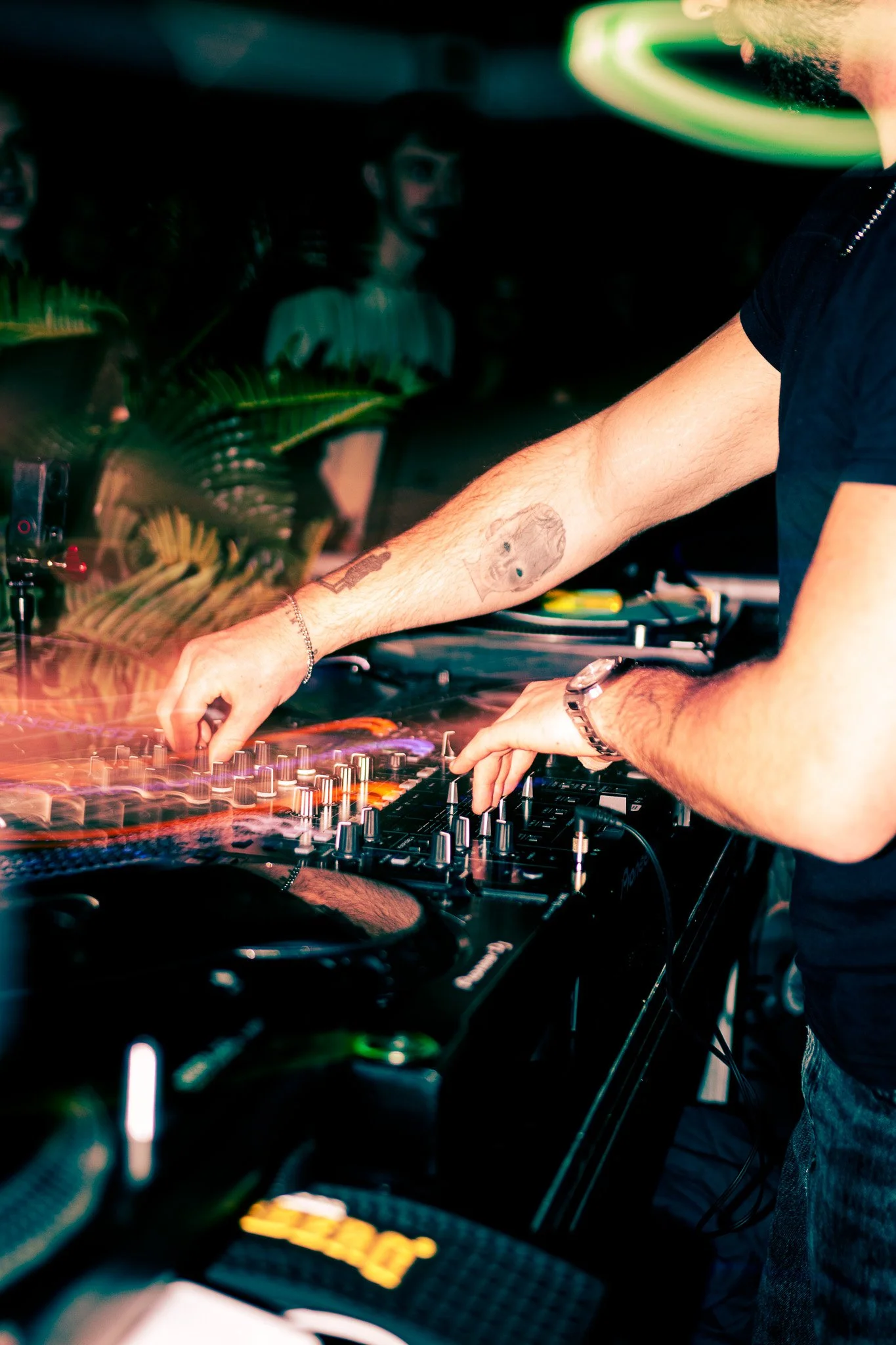 A DJ mixing music with a turntable at a nightclub, with people dancing in the background.