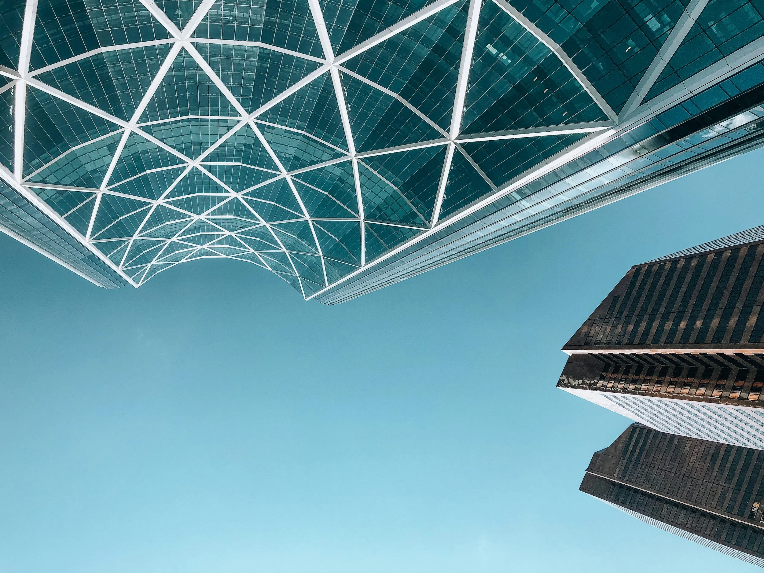 Looking up at tall modern skyscrapers with glass facades against a clear blue sky.