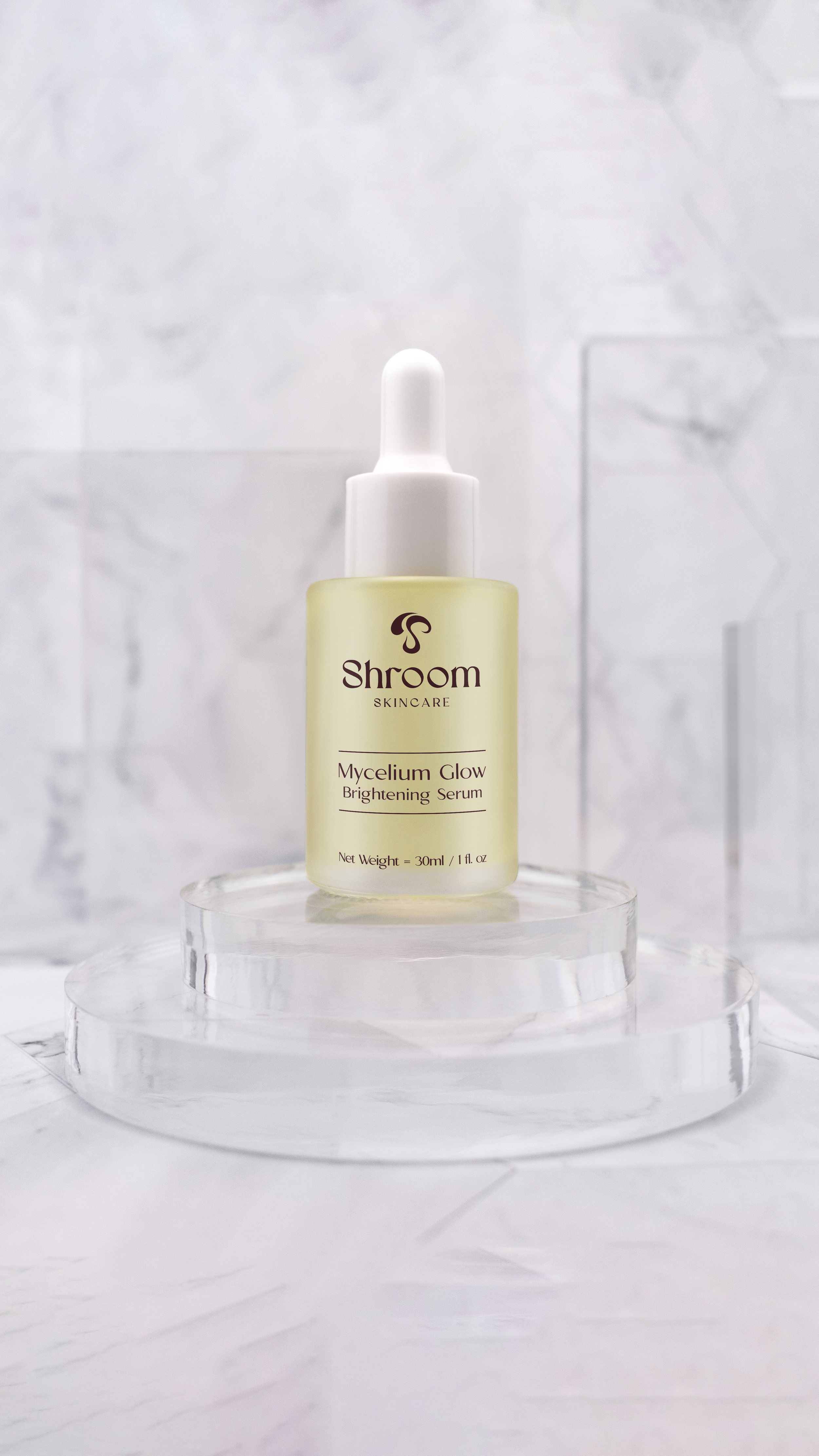 A small bottle of Shroom Skincare Mycelium Glow Brightening Serum with a white dropper cap, placed on a clear acrylic stand against a marble background.