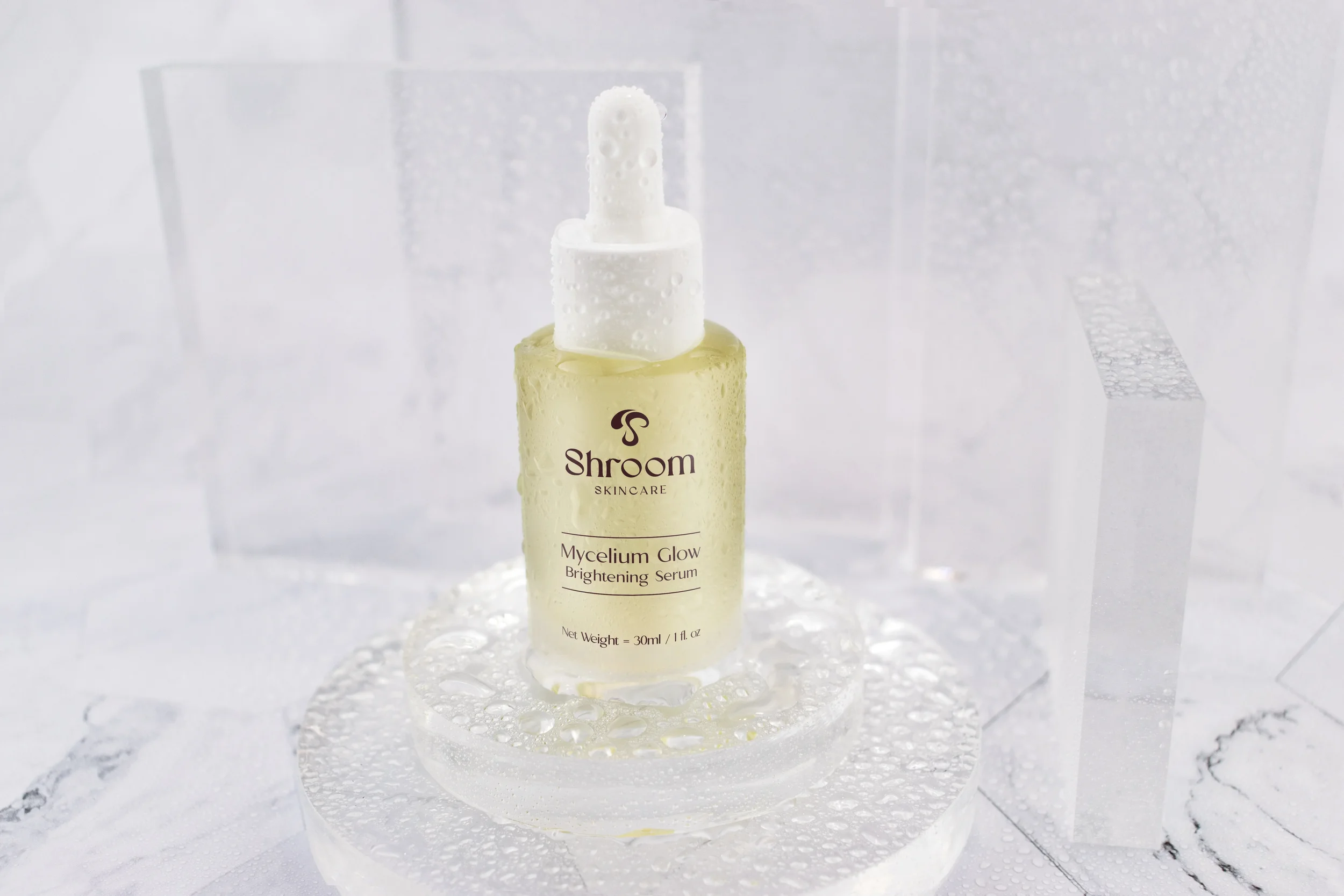 Water droplet-covered Mycelium Glow serum bottle on marble surface