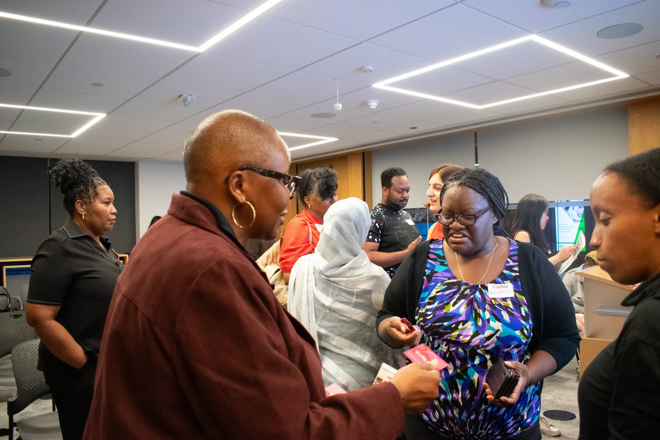 A group of diverse people gather around a table in a modern indoor space, engaging in conversation and exchange of documents or tickets.