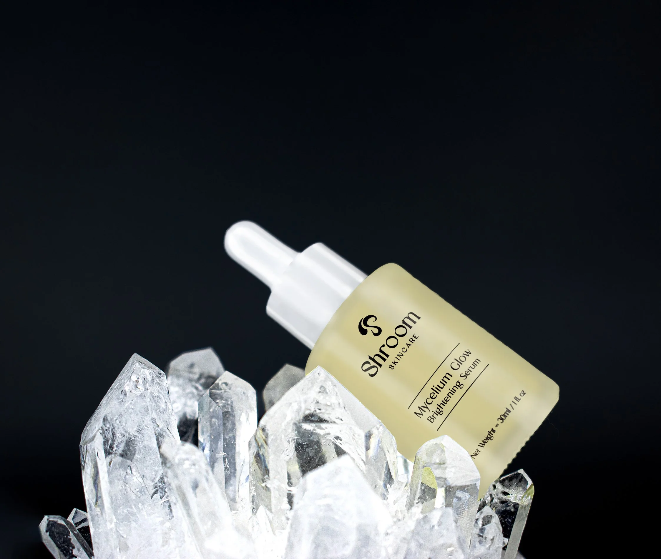 A bottle of ShrooM Skincare's Mycelium Glow Brightening Serum surrounded by clear crystal stones on a black background.