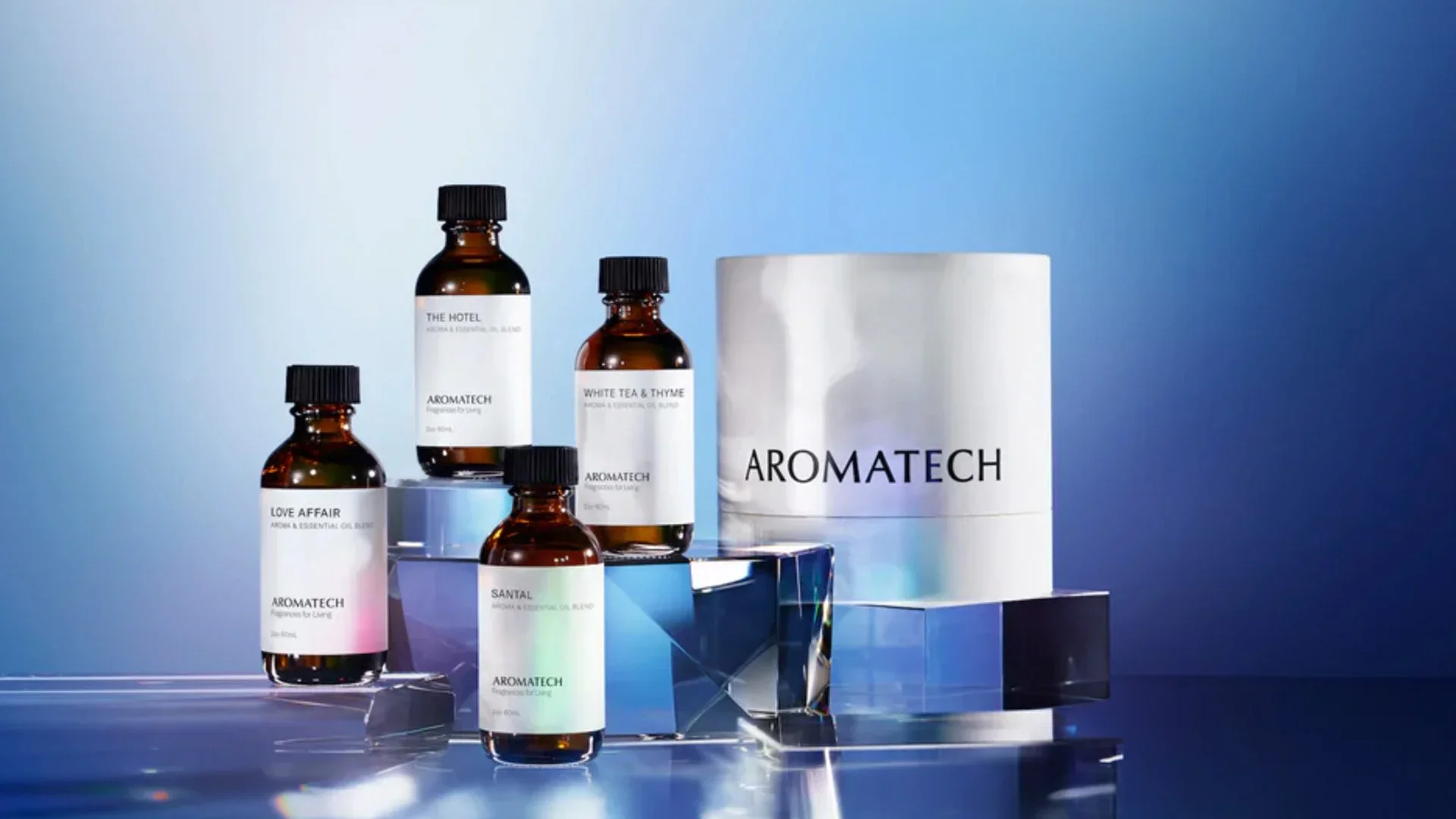 Collection of AROMATECH essential oil bottles with white labels, placed on glass and acrylic stands against a gradient blue background.