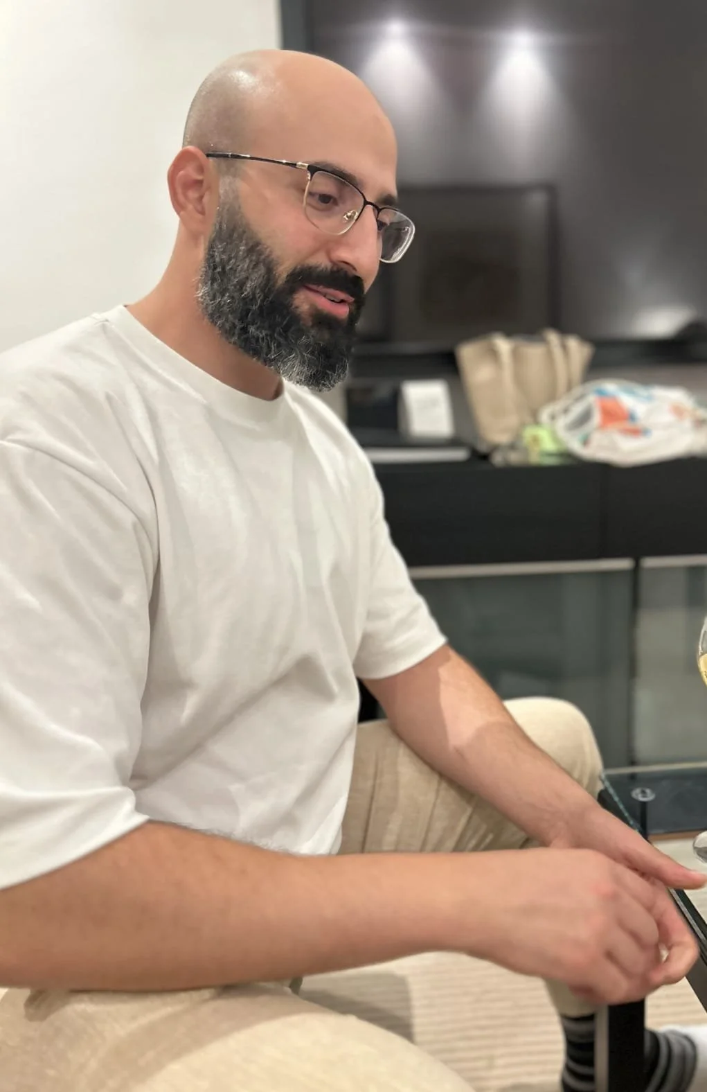 A bald man with a beard and glasses wearing a white t-shirt sitting at a table.