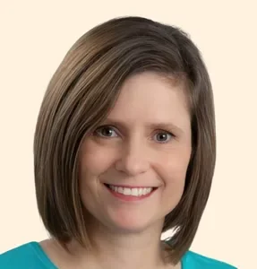 Close-up of a woman with shoulder-length brown hair wearing a teal top and smiling, against a neutral background.