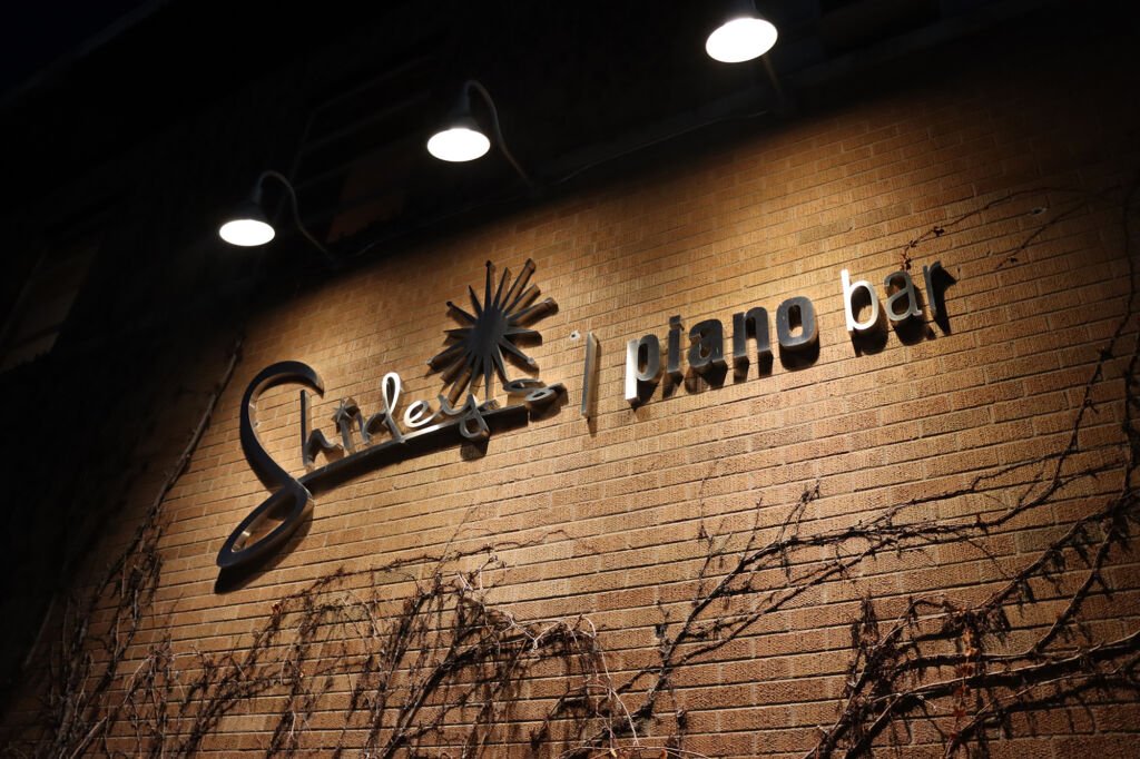 Sign for Sloley's Piano Bar on a brick wall with lighting above