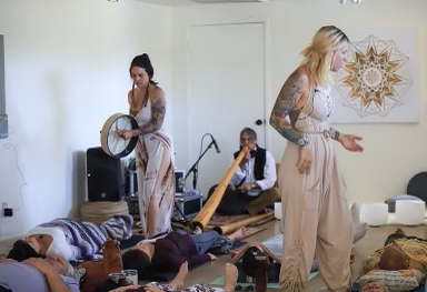 Three women performing a sound bath in a room with people lying on mats and blankets.