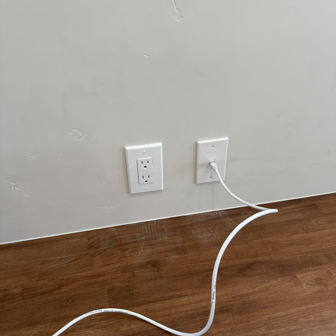 Empty wall with electrical outlet and network cable connected to an Ethernet port.