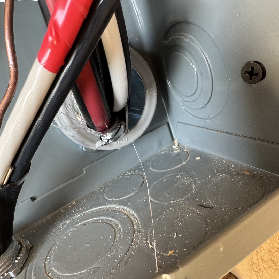 Inside an electrical panel with wires and a loose open screw on the gray metal surface.