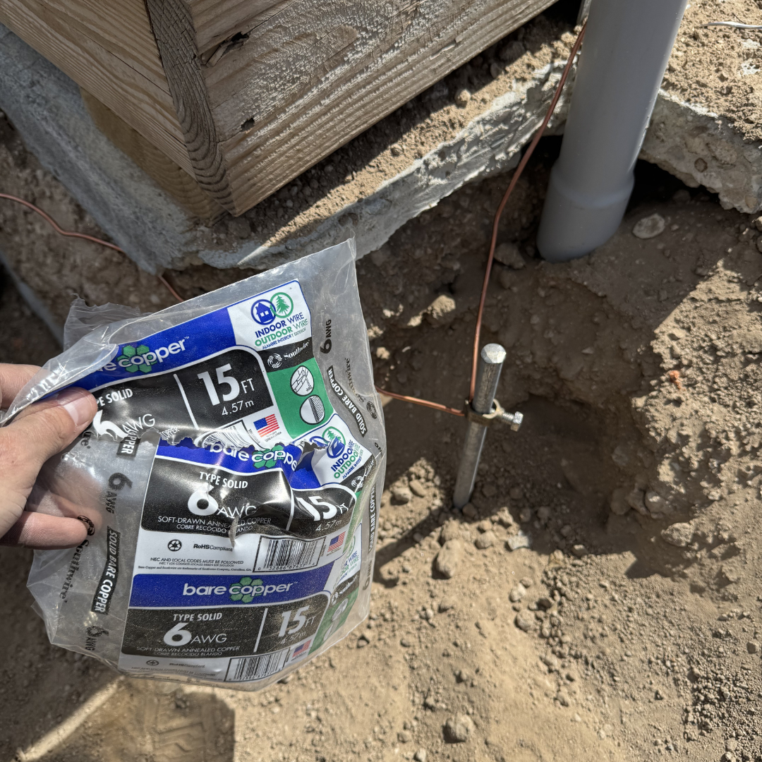 Construction site with a person holding a bag of 6-gauge solid copper wire near a metal post and pipe installed in the ground.