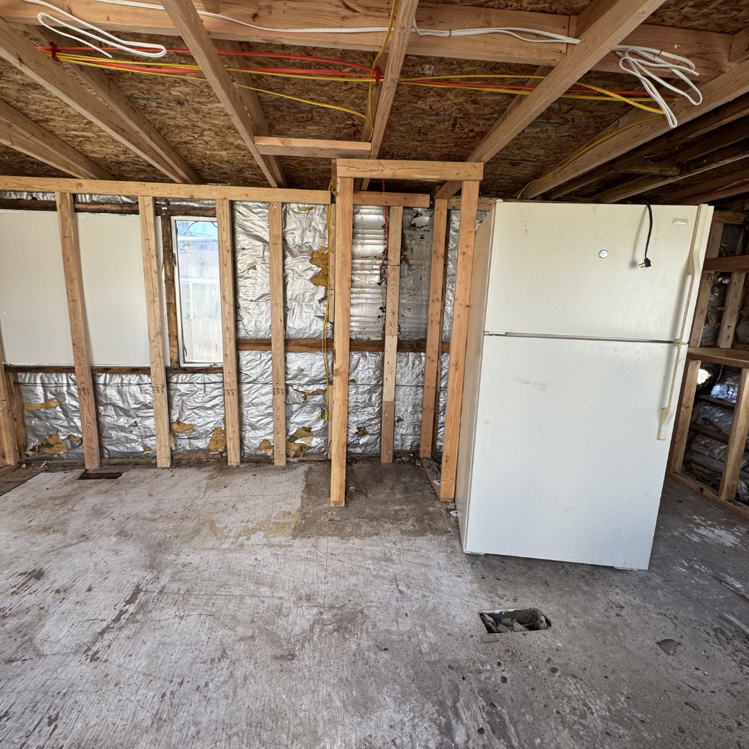 Unfinished room with exposed wooden framing, insulation, a small window, and a white refrigerator.