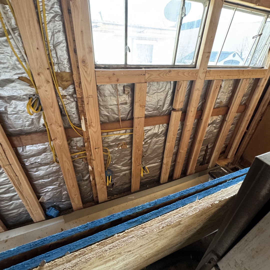 Interior view of a house under construction showing wooden framing, insulation, and a window.