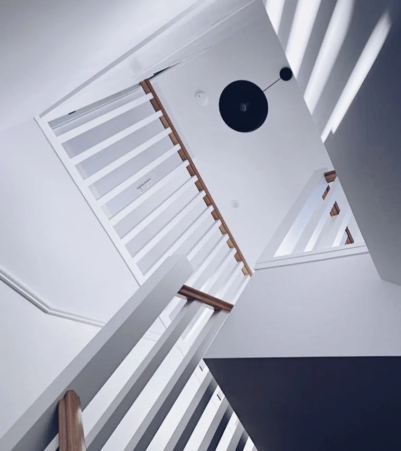 View of a modern, white staircase with wooden handrails from below, capturing the geometric lines and angular design of the staircase and ceiling.