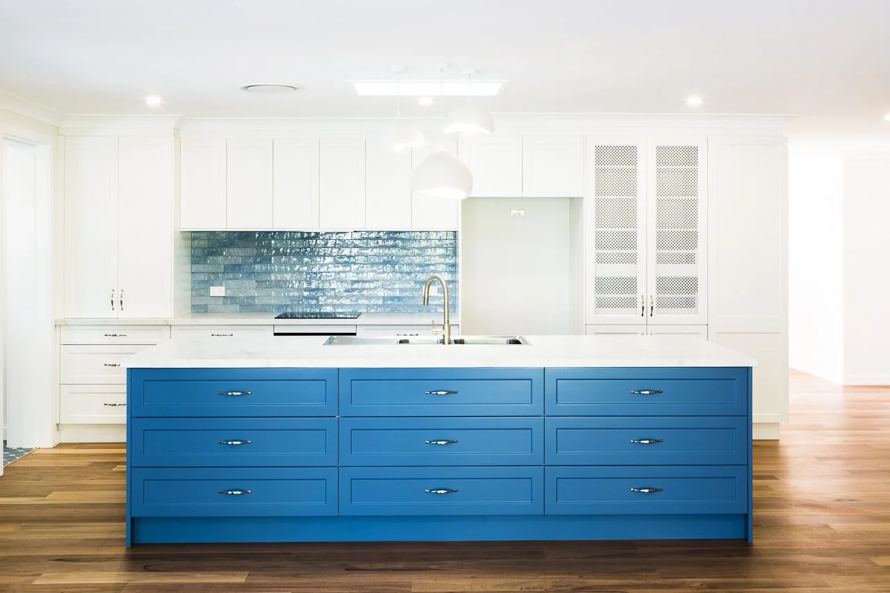 Modern kitchen with a blue island, white cabinets, blue backsplash, and wooden floors.