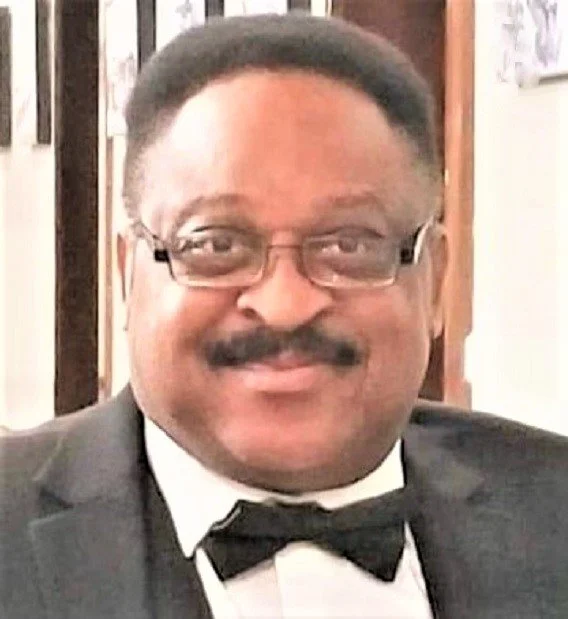 A man with glasses, a mustache, wearing a tuxedo with a bow tie, smiling.