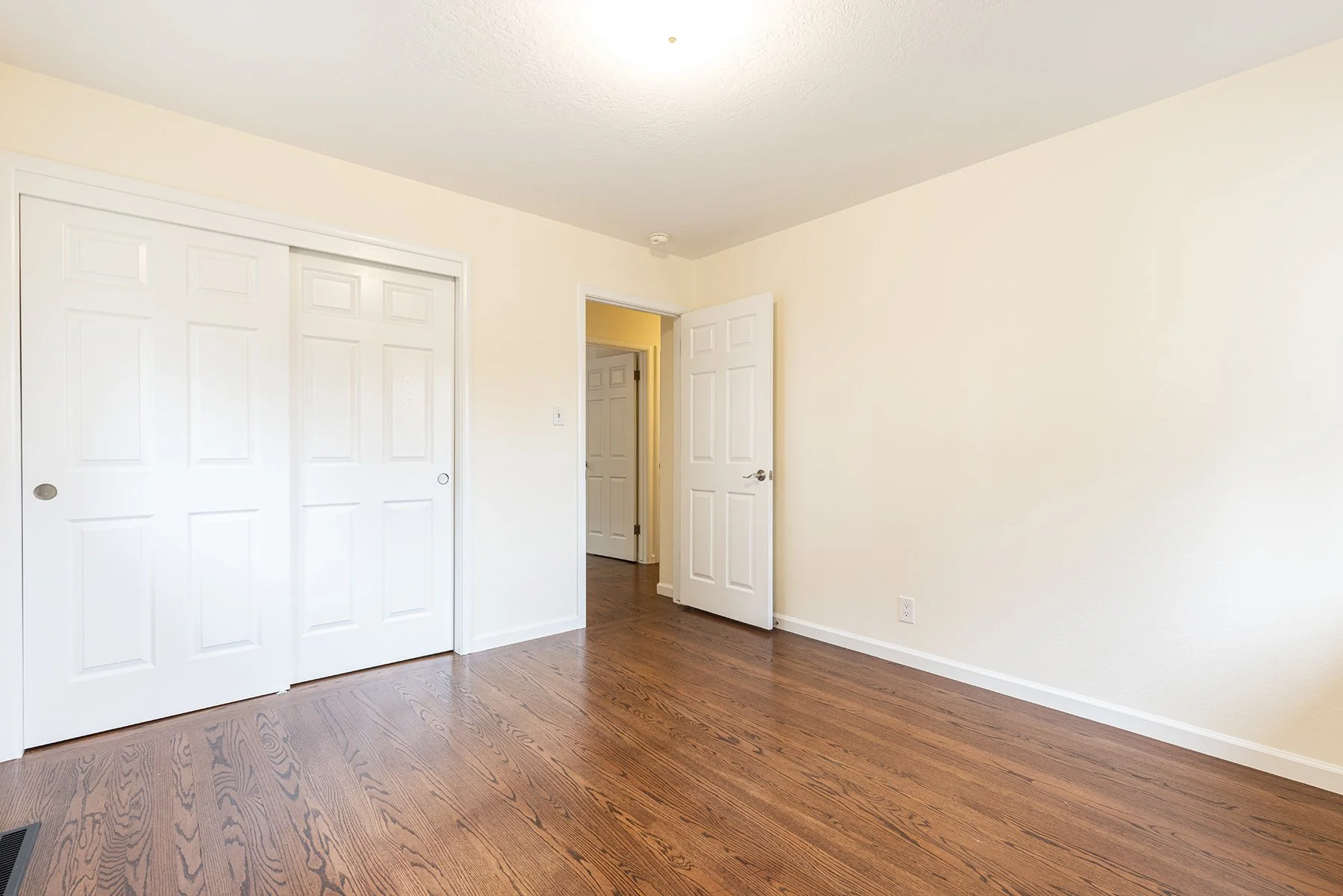 Empty room with hardwood floors, closed closet doors, an open doorway, and beige walls