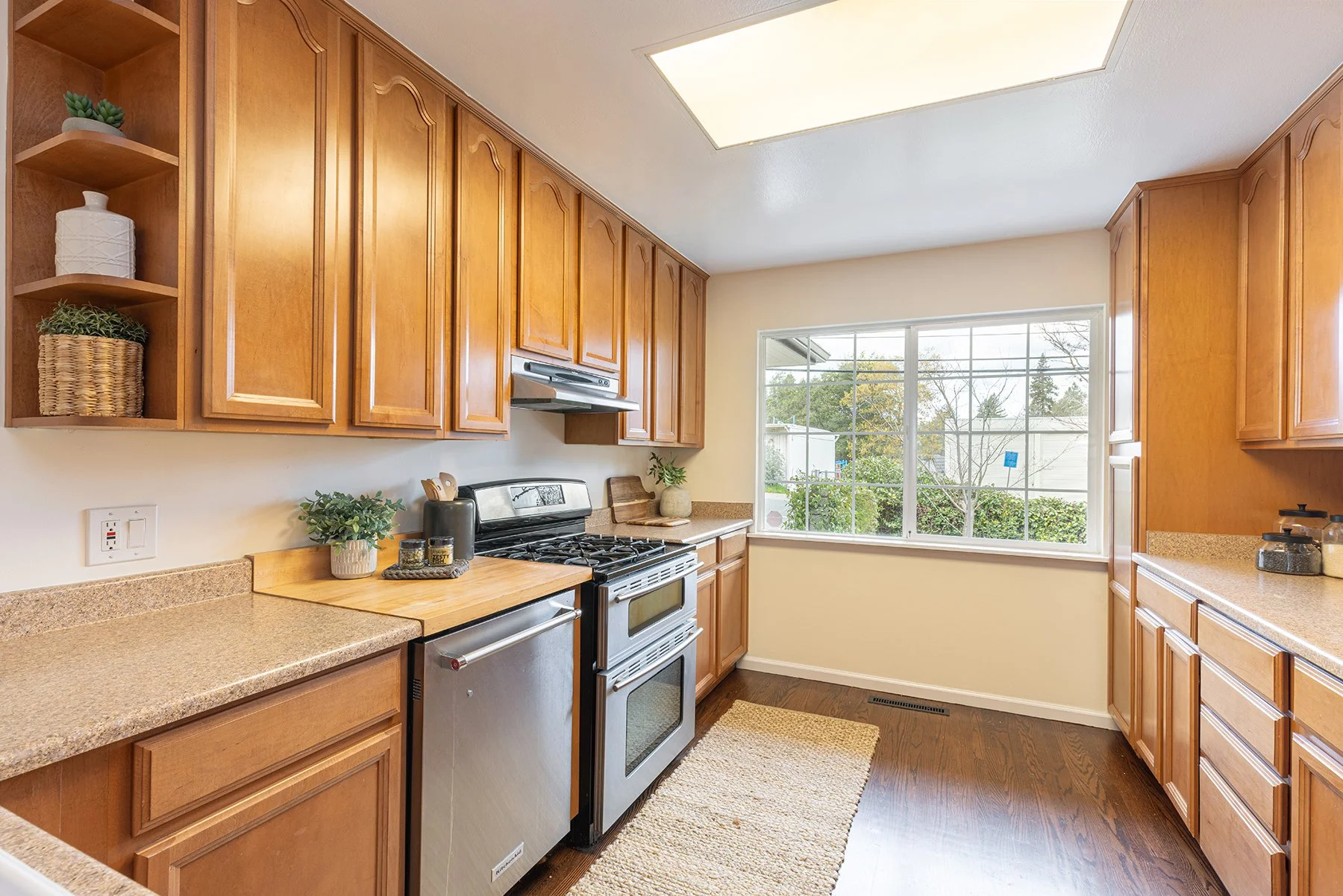 Kitchen with wooden cabinets, stainless steel stove, granite countertops, a window showing outdoor scenery, and decorative plants.