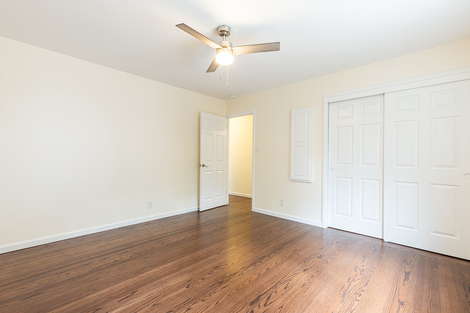 Empty bedroom with hardwood floors, white walls, a ceiling fan, and a closet with sliding doors.