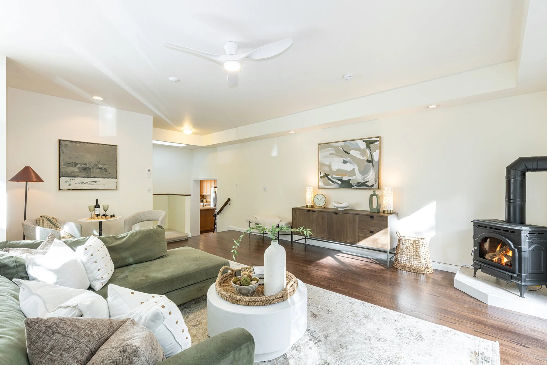 Living room with a green sofa, white pillows, a wooden sideboard, a wood-burning stove, and a ceiling fan.