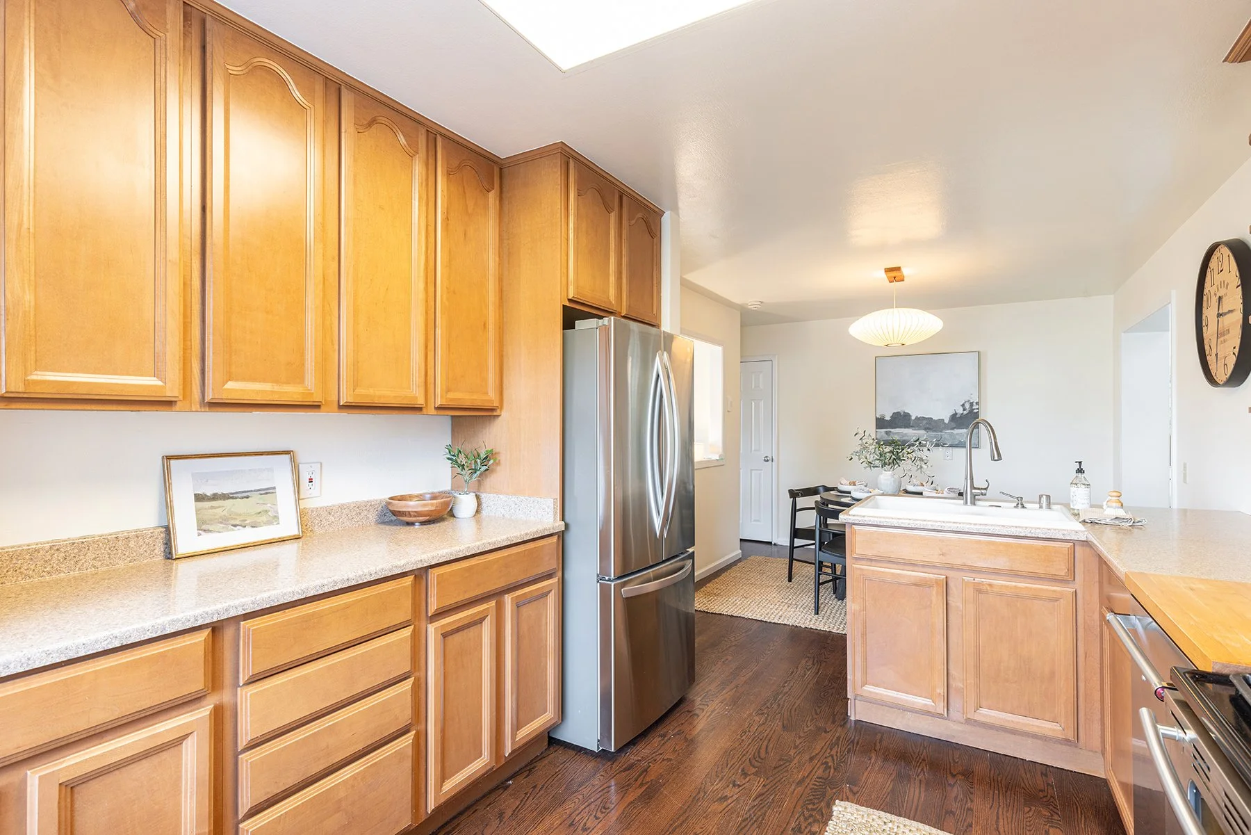 Kitchen with wooden cabinets, stainless steel refrigerator, granite countertops, and a dining area with black chairs and a table.