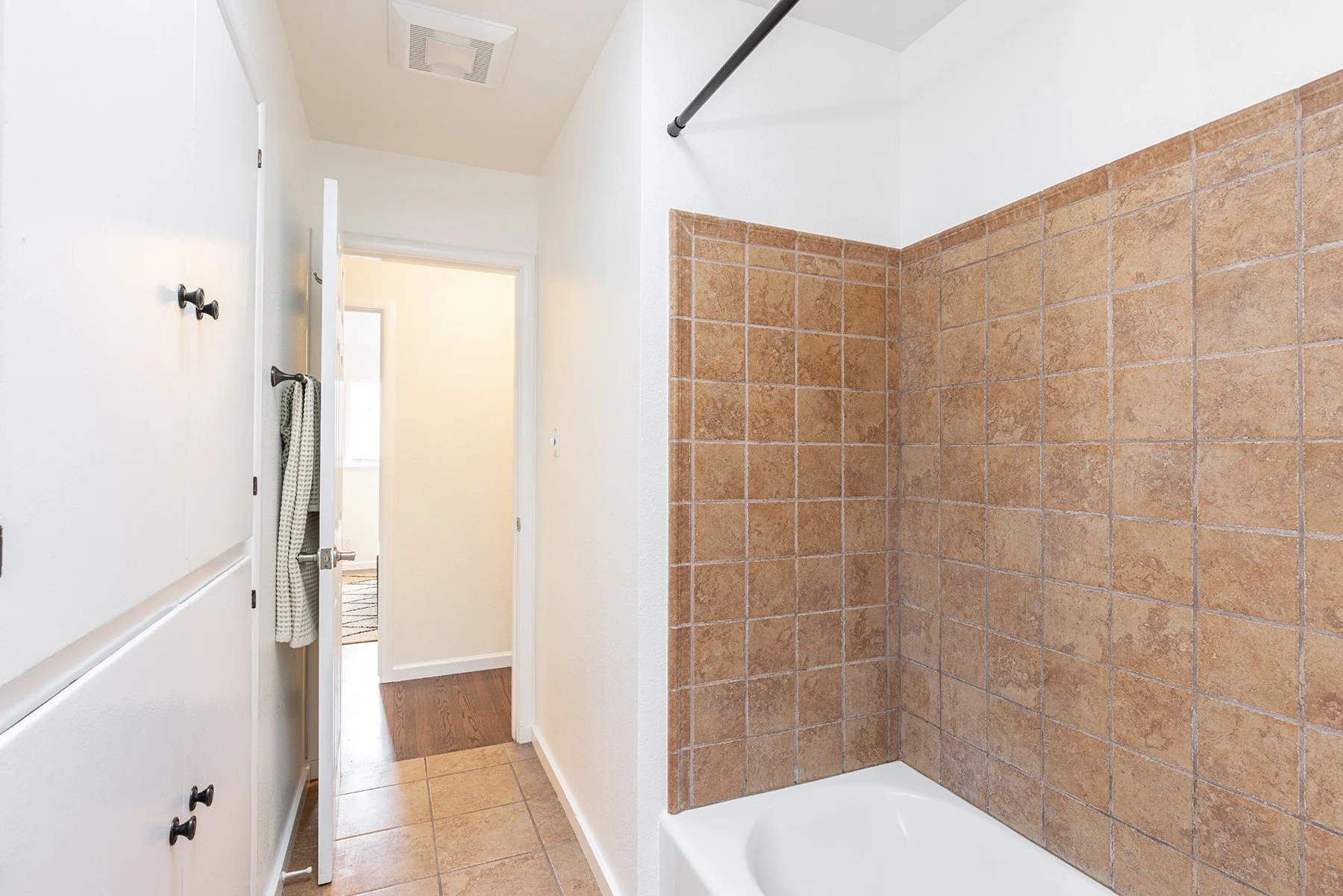 Bathroom with a walk-in shower featuring brown tile walls, white bathtub, white walls, white door with a towel hanging, and a ceiling vent.