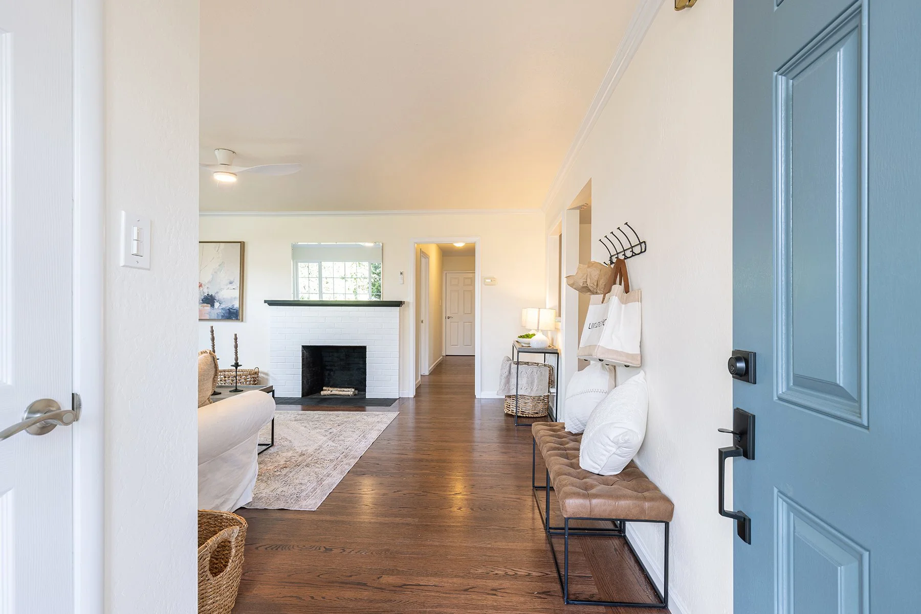 View of a cozy living room with a white fireplace, wooden floors, and a blue front door.