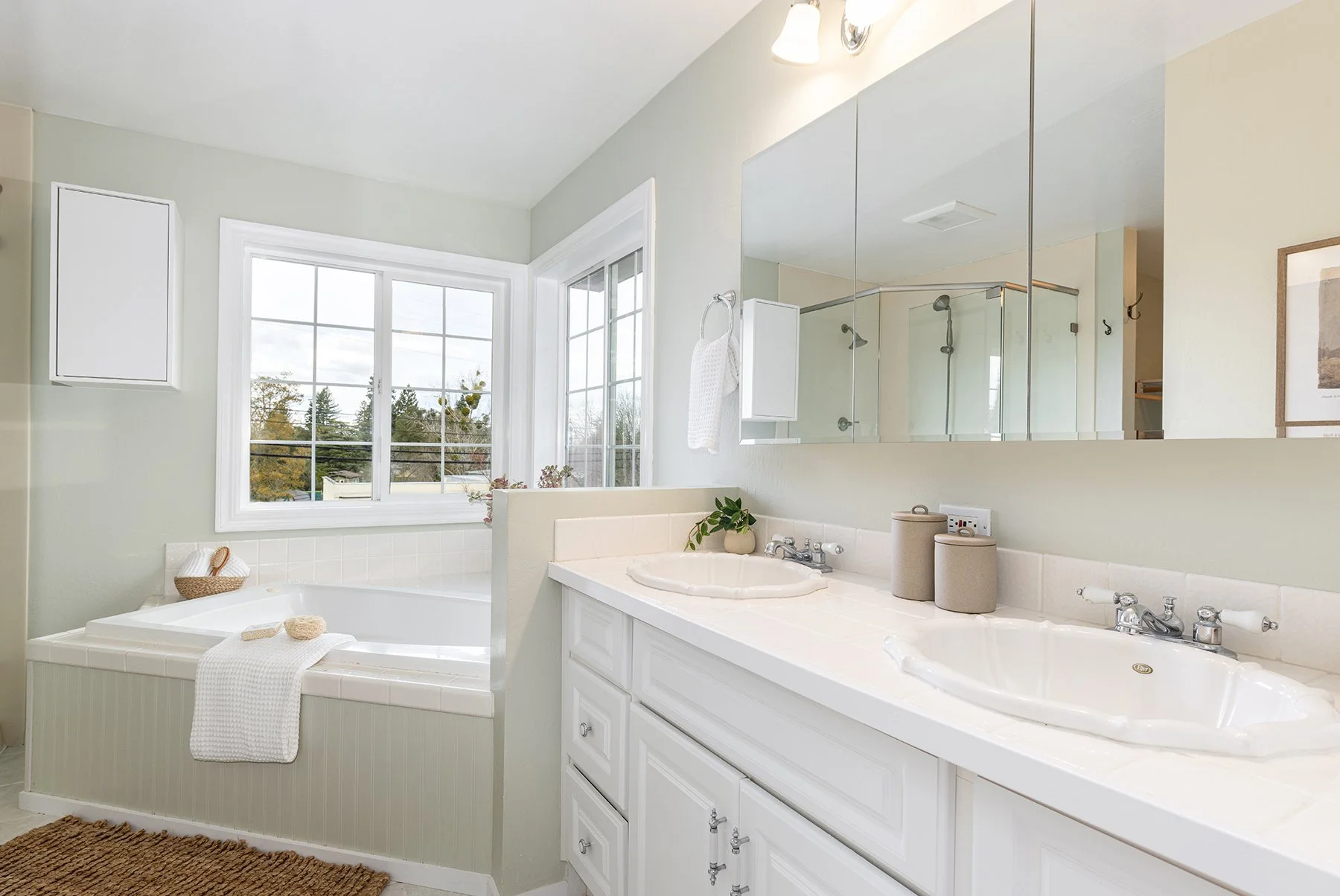 Bright bathroom with a large window, double sinks, a mirror, a bathtub, and neutral decor.
