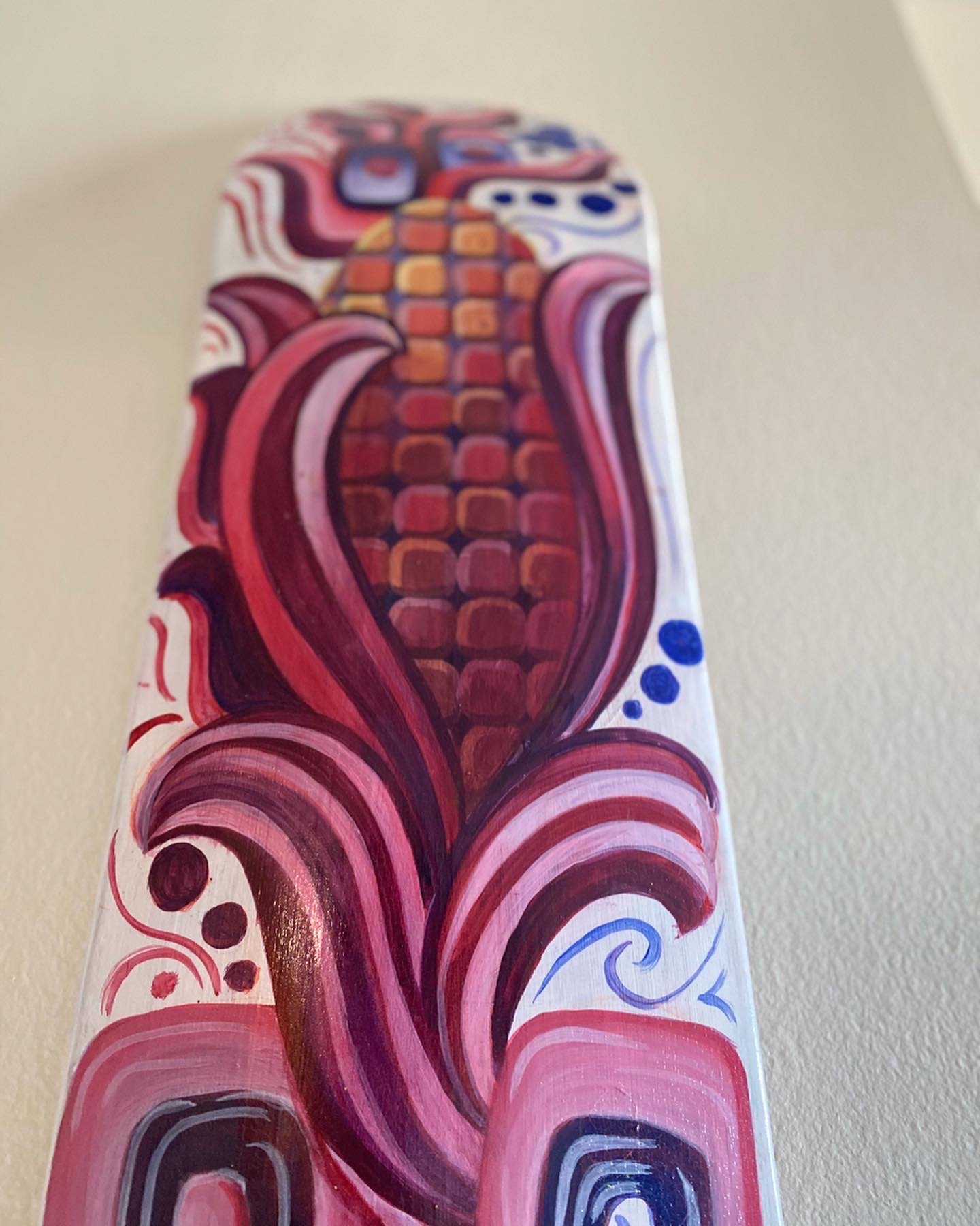 Close-up of a colorful abstract painting featuring red, pink, purple, blue, and orange shapes, including what appears to be a pineapple and swirling patterns on a white background.