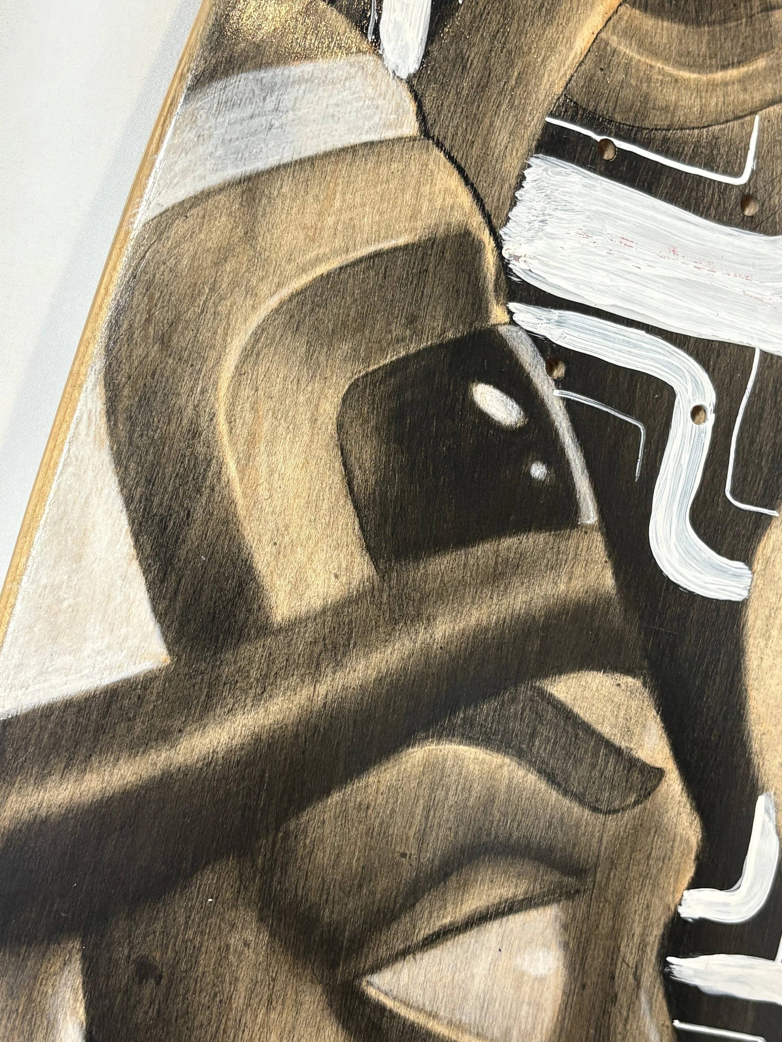 A close-up of a wooden artwork featuring a stylized face with abstracted features and white paint accents.