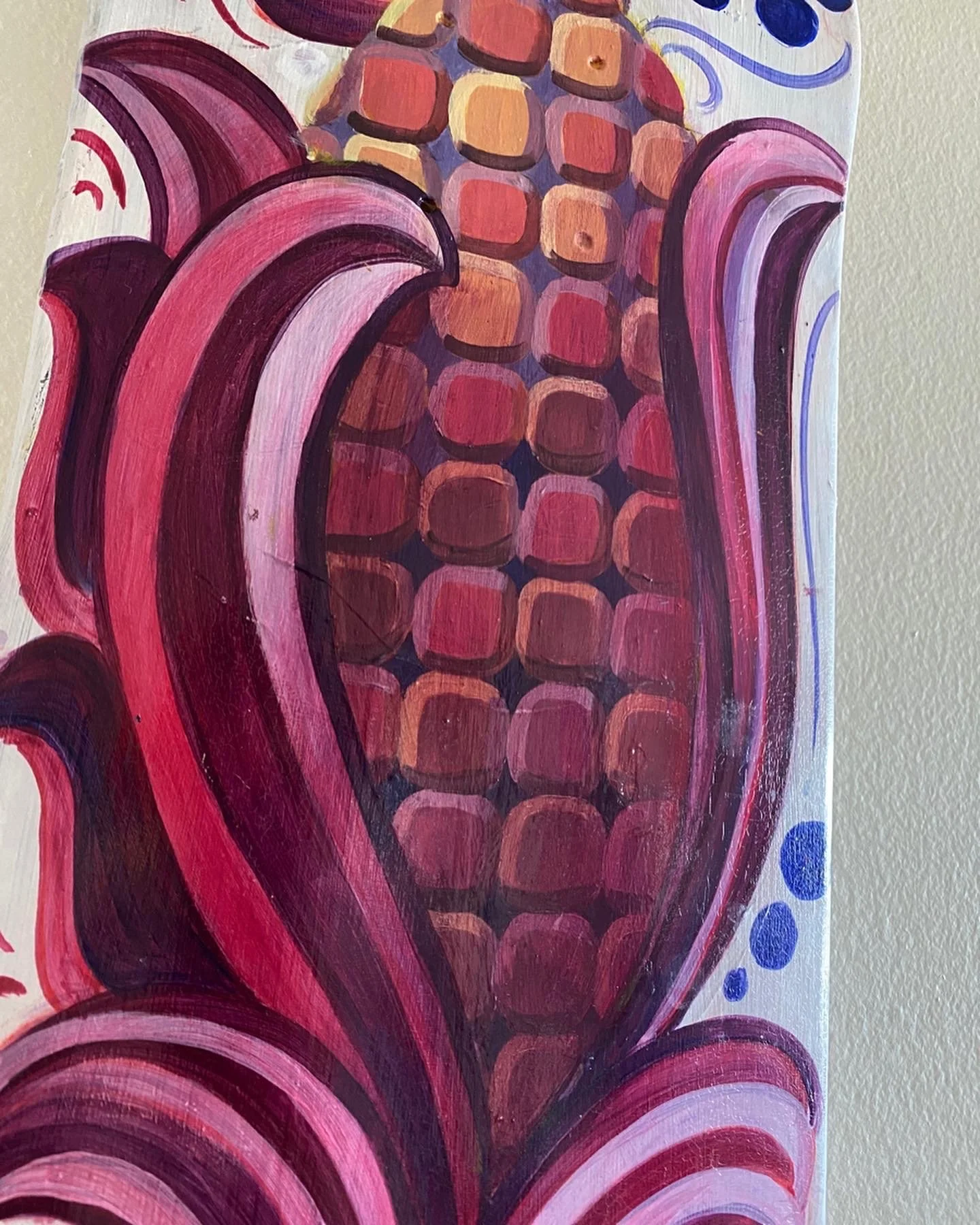 Close-up of a colorful, abstract painting of a corn cob with pink and purple husks, and a yellow and red kernels on the cob.