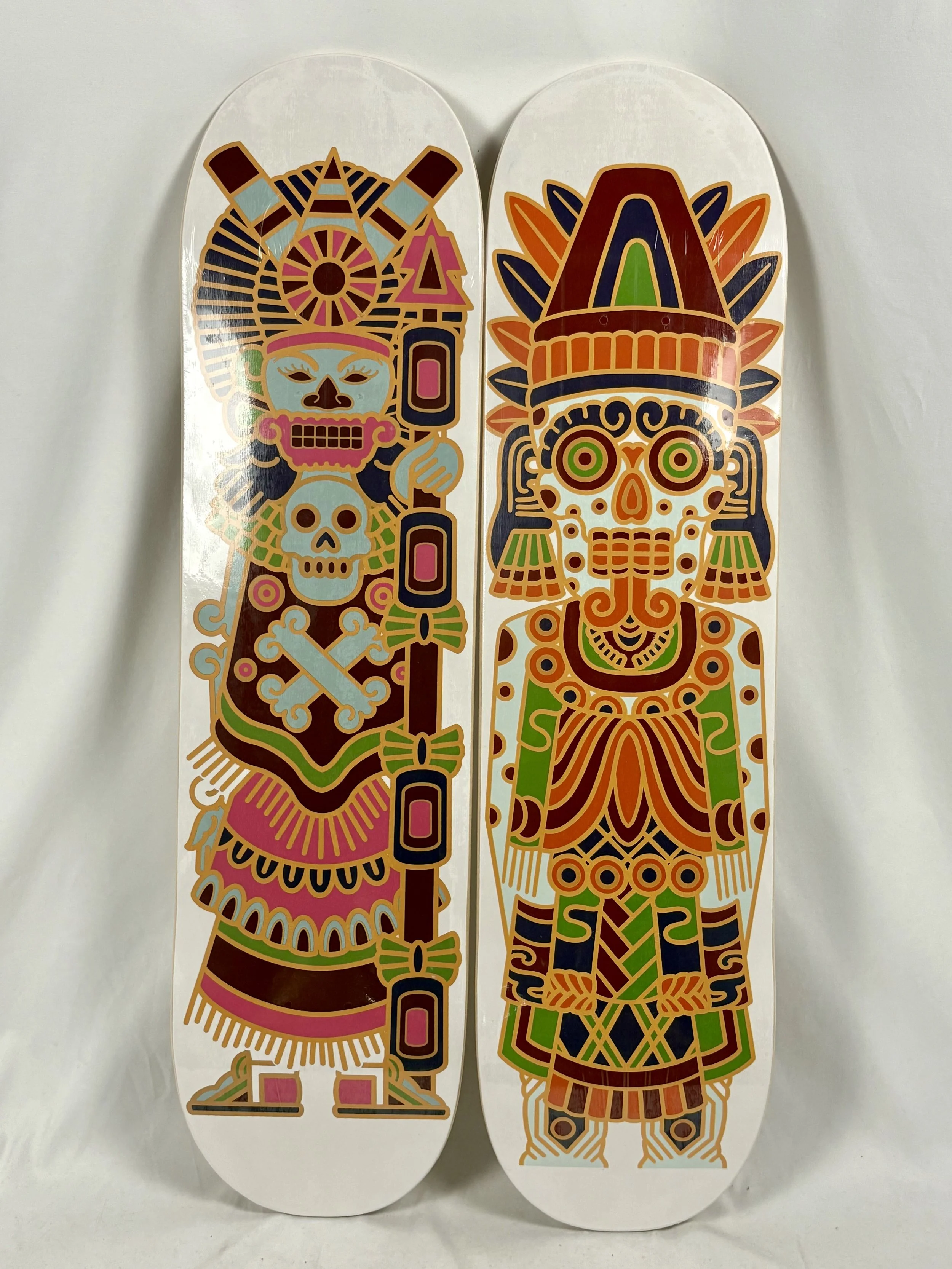 Two skateboard decks with colorful, indigenous-inspired artwork depicting stylized human figures with elaborate headdresses and face paint.