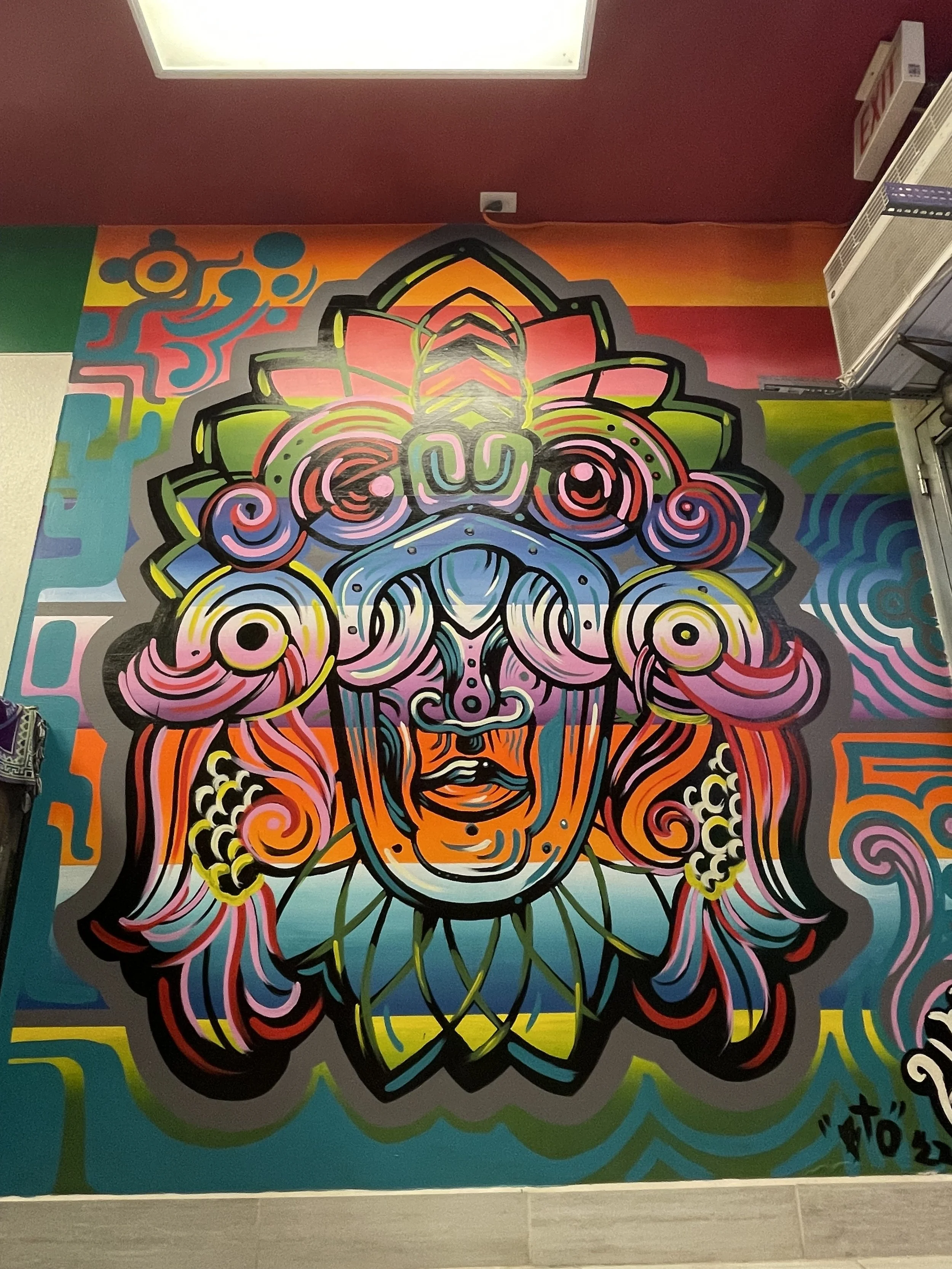 Colorful mural of a stylized face with intricate patterns, bold lines, and vibrant colors on a wall.